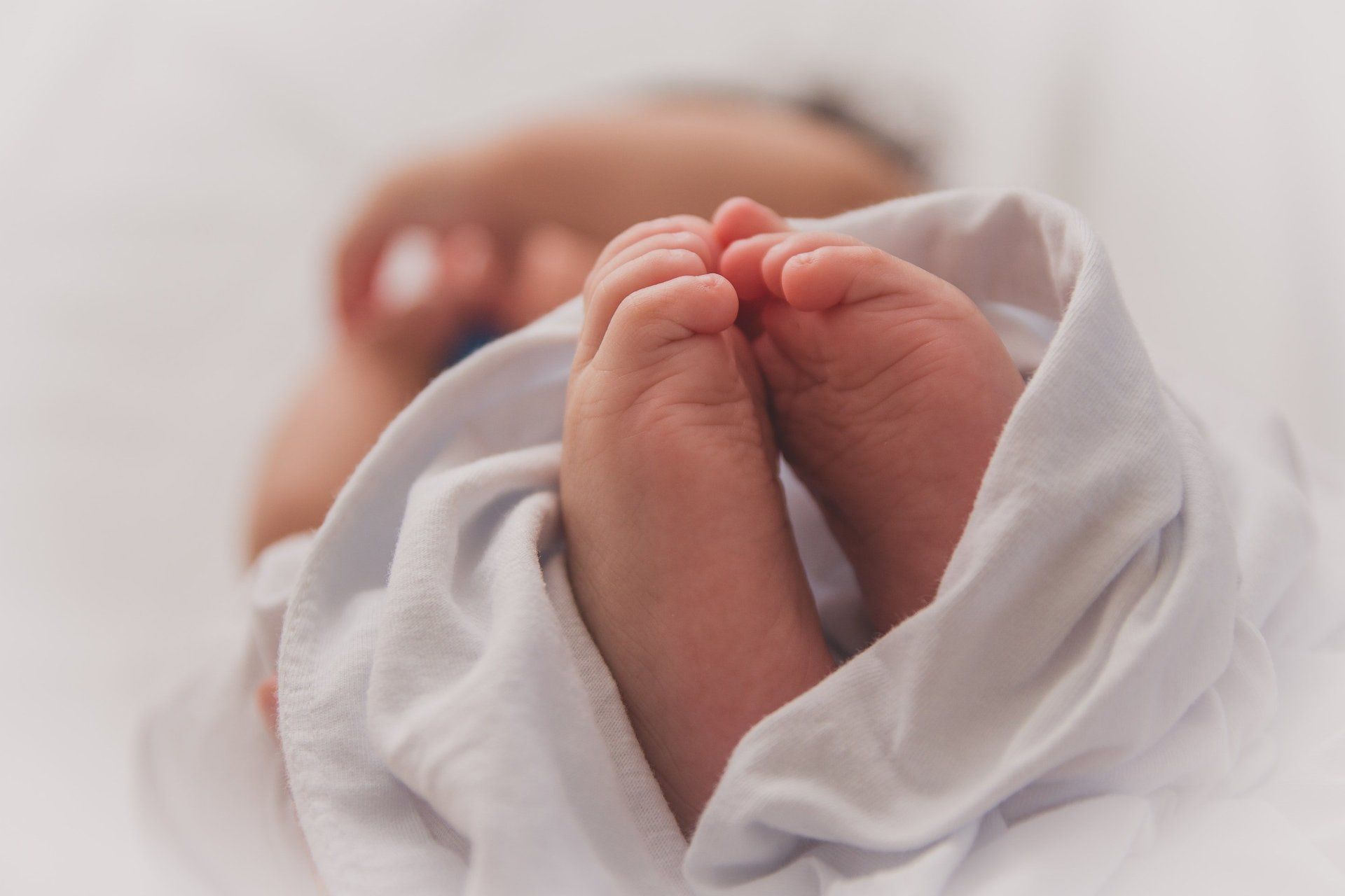 Close-up of a newborn baby's tiny feet swaddled in a white blanket.