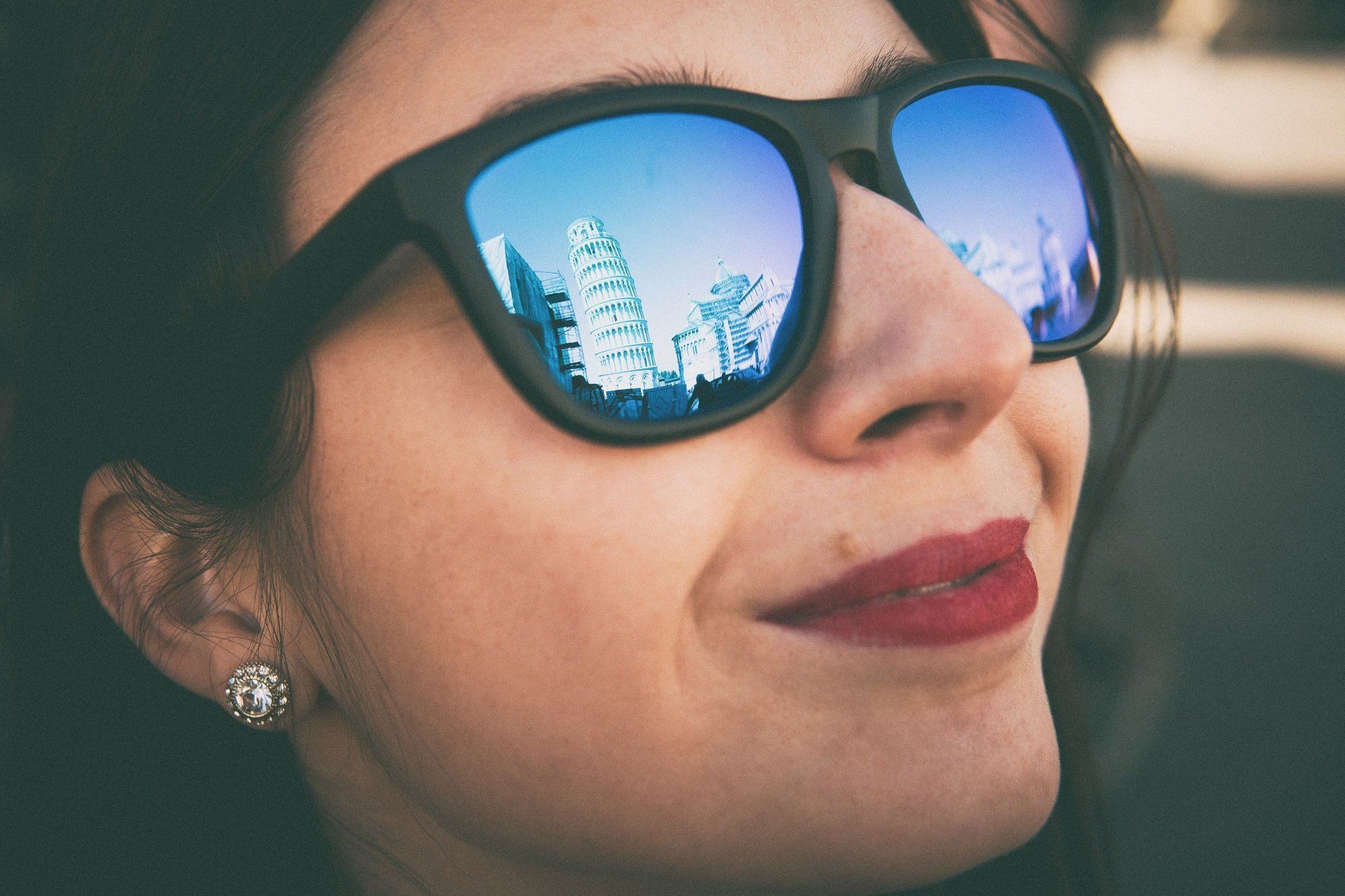 Una donna che indossa occhiali da sole sorride con il riflesso di una città nei suoi occhiali da sole.