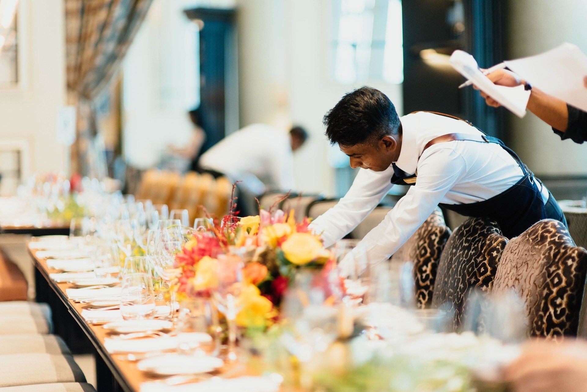 A waiter is setting a long table in a restaurant.
