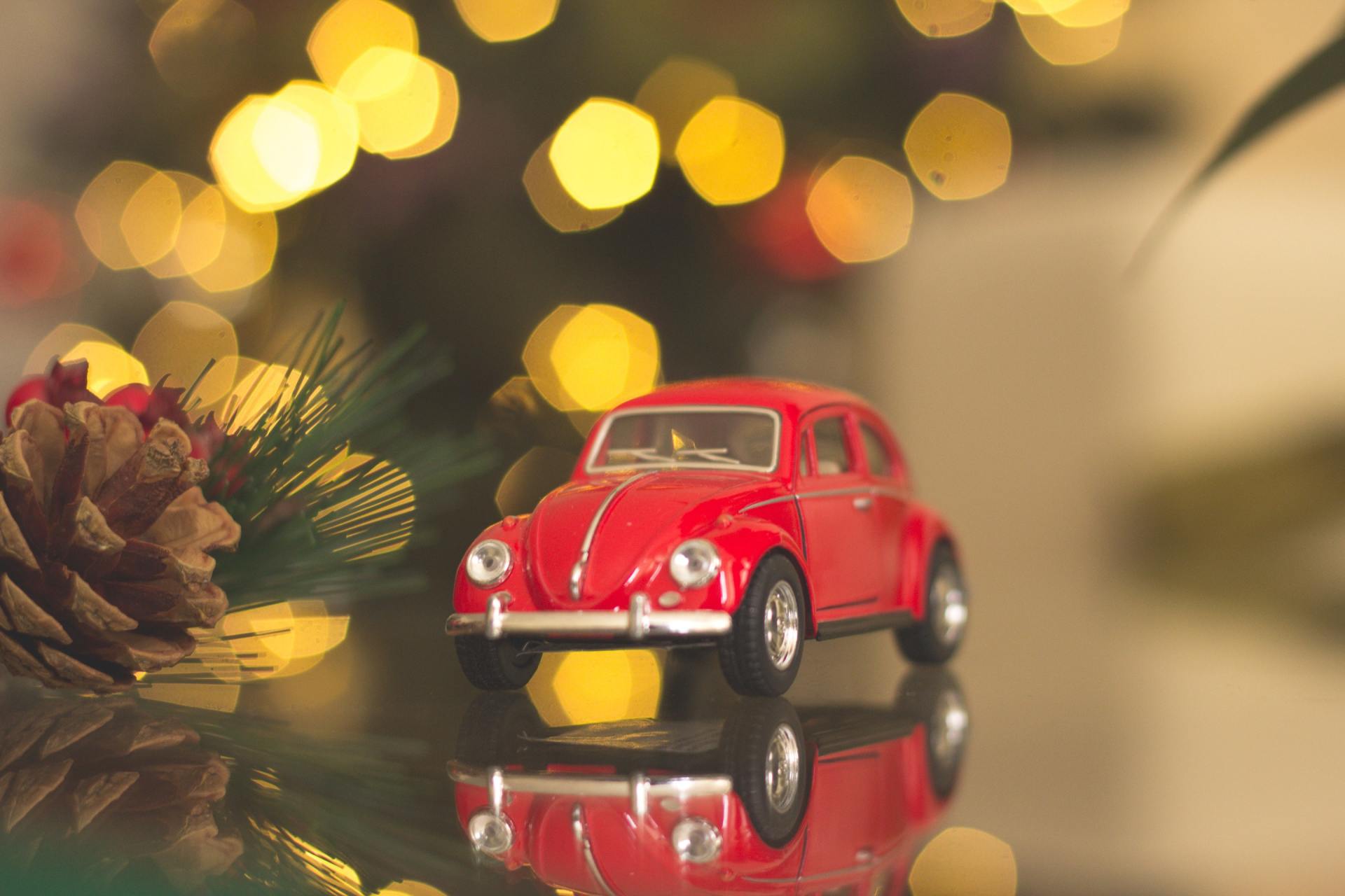 Neben einem Tannenzapfen und einem Weihnachtsbaum steht ein rotes Spielzeugauto.