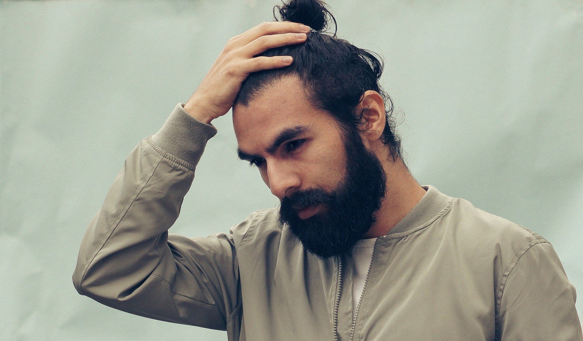 A man with a beard is holding his hair in a bun.
