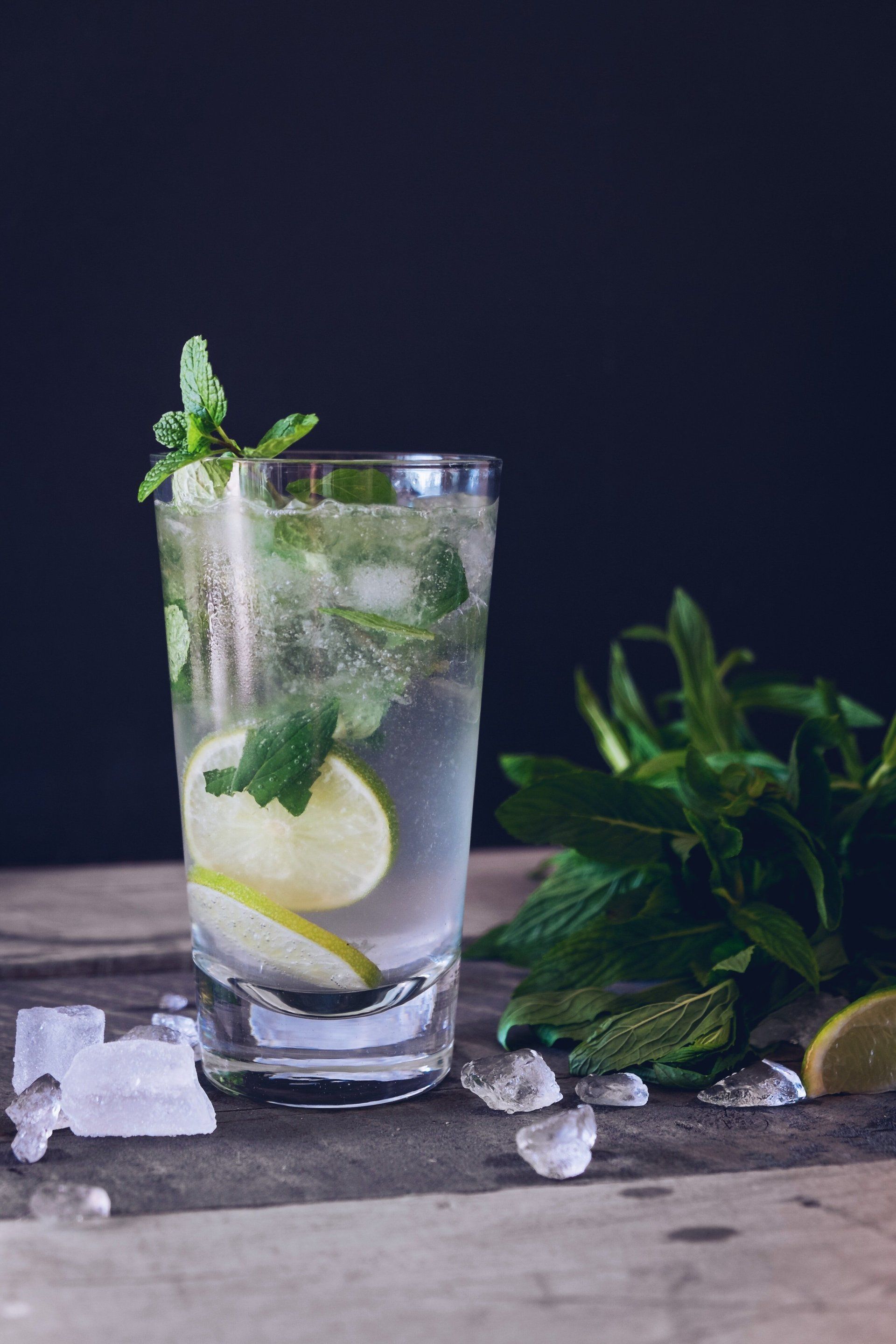 Mint and lemon iced drink in a glass with crushed ice on a rustic table, with herbs beside it.