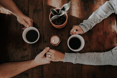 A man and a woman are sitting at a table holding cups of coffee.