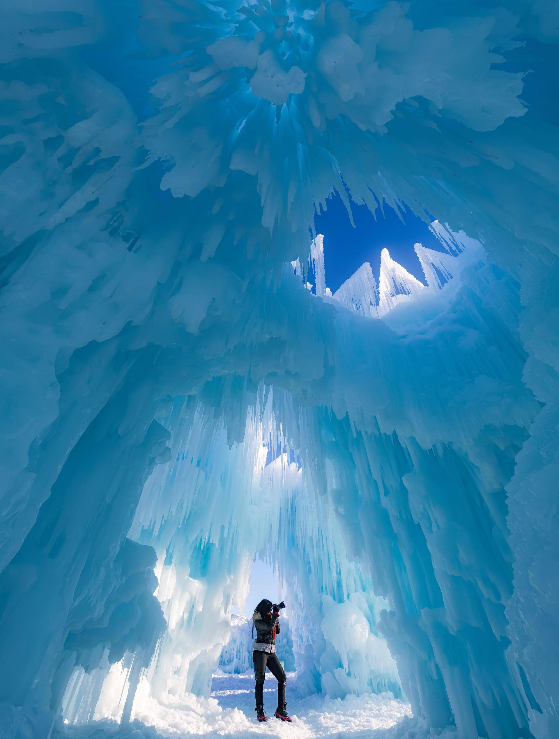 Eine Person steht in einer blauen Eishöhle mit leuchtenden, zerklüfteten Eiswänden.