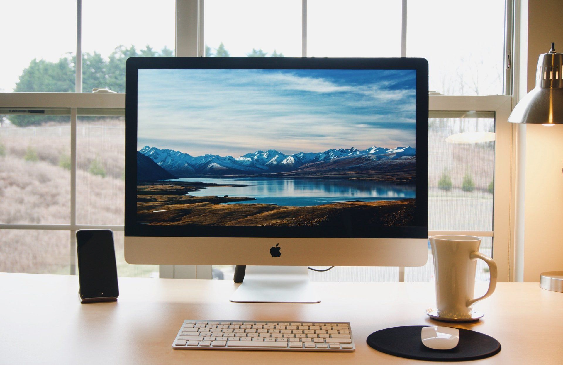 Una computadora Apple está colocada sobre un escritorio frente a una ventana.