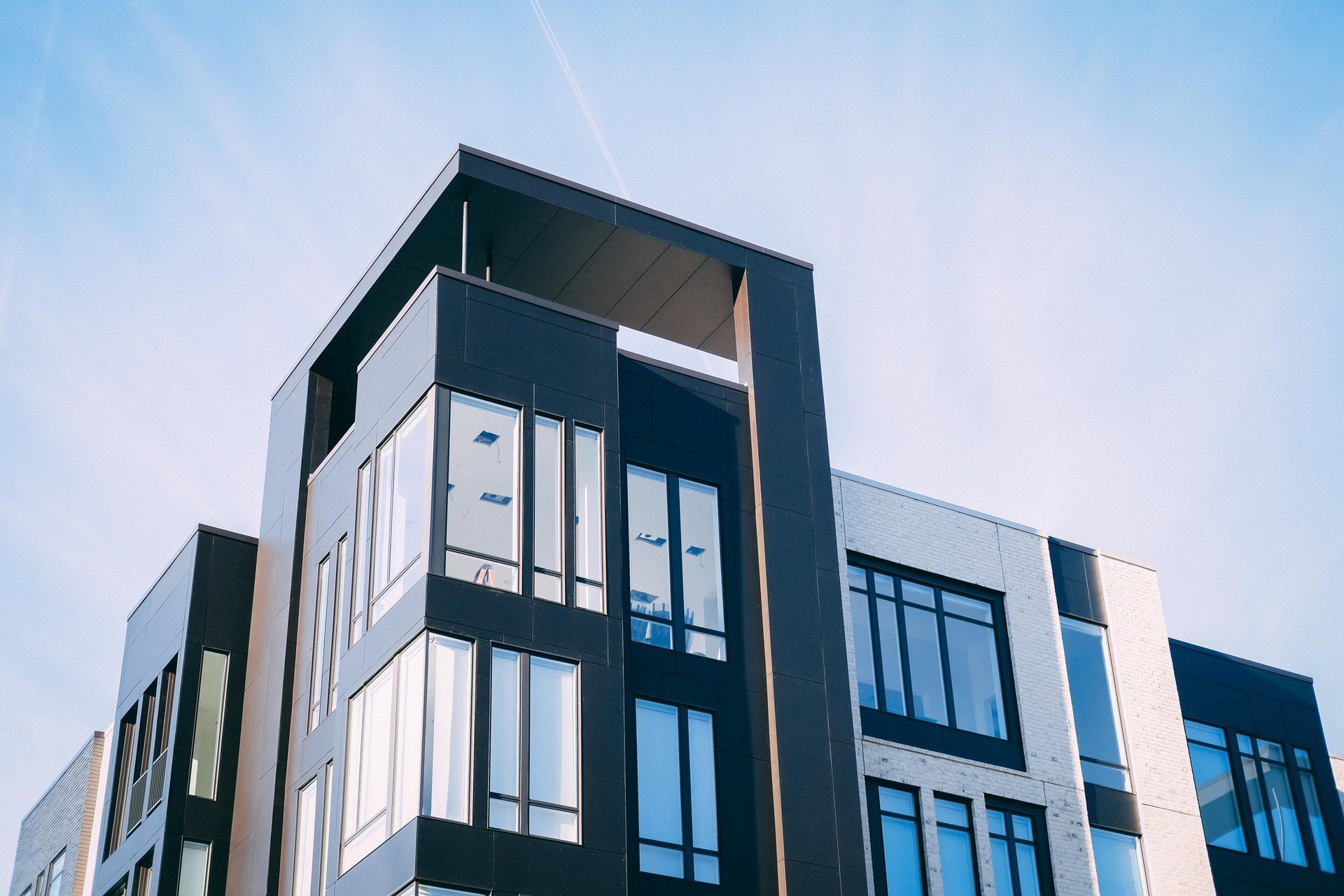 Modern multi-story building with dark exterior and large windows against a blue sky.