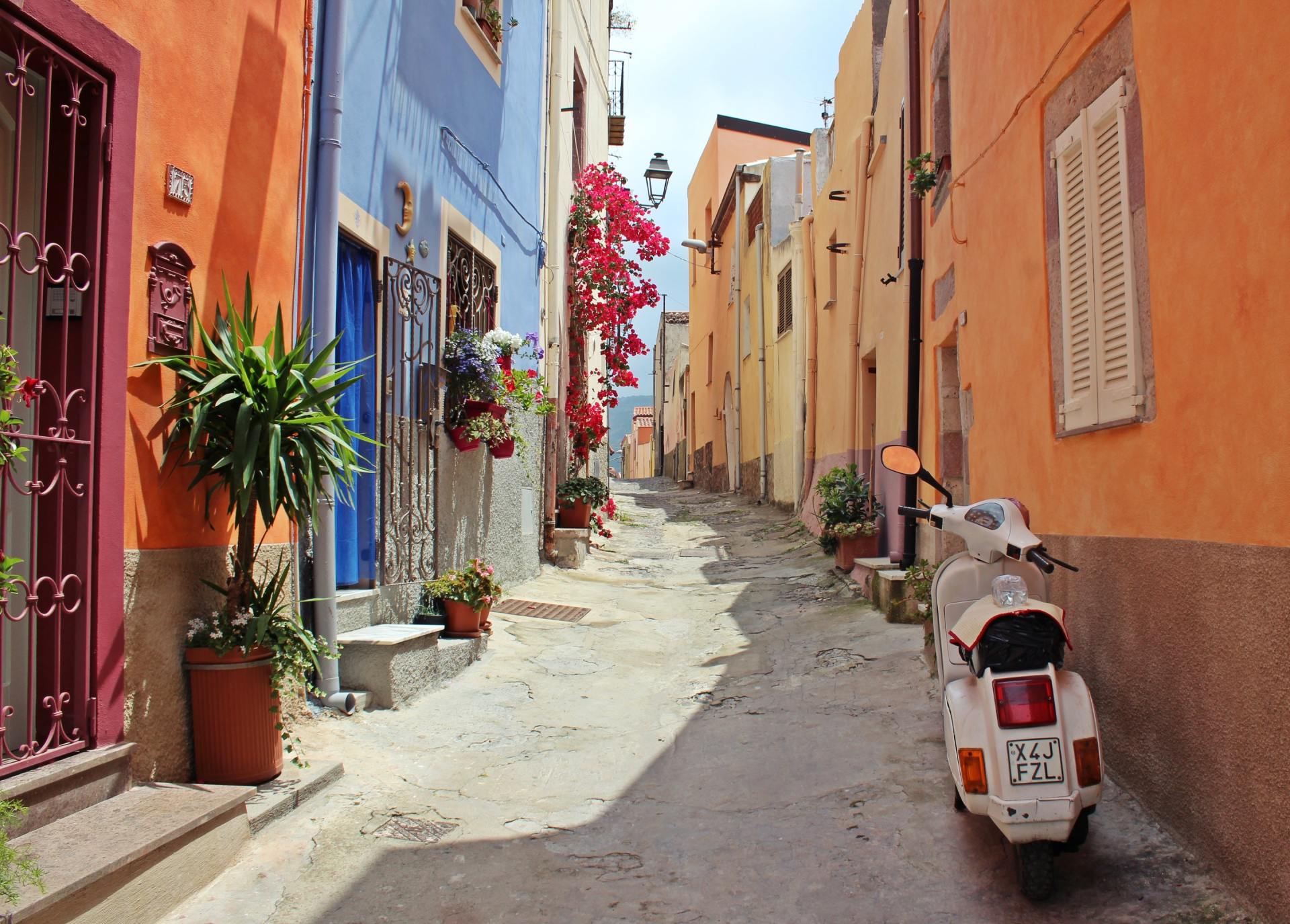 A scooter is parked on the side of a narrow street