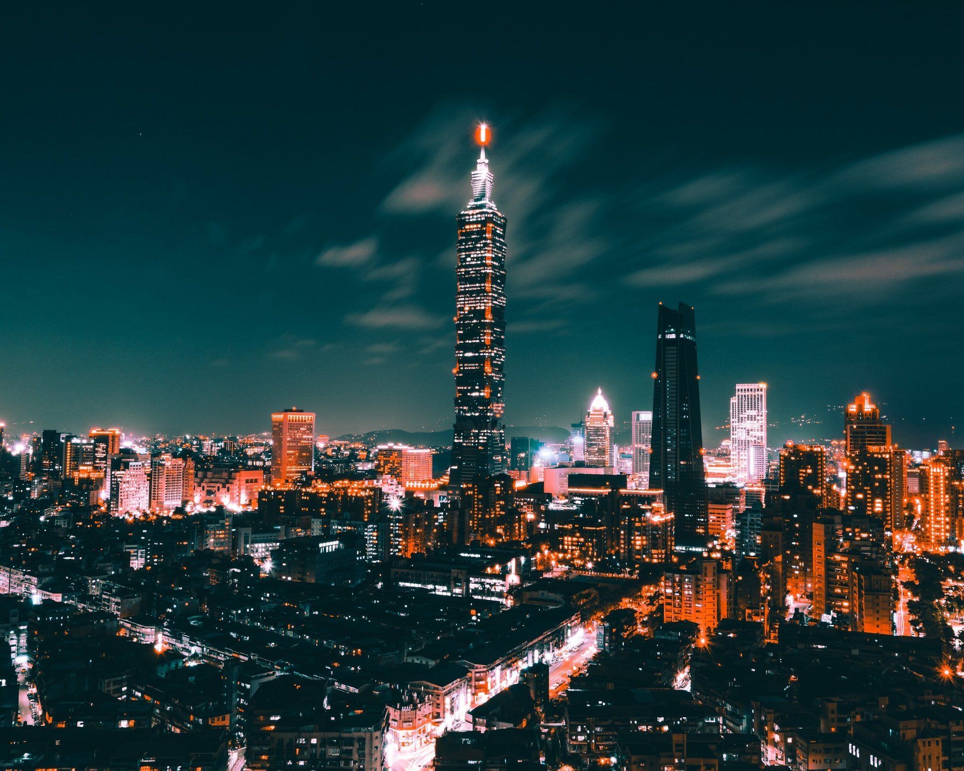 Night view of Taipei cityscape with illuminated skyscrapers, including Taipei 101, under a dark teal sky.
