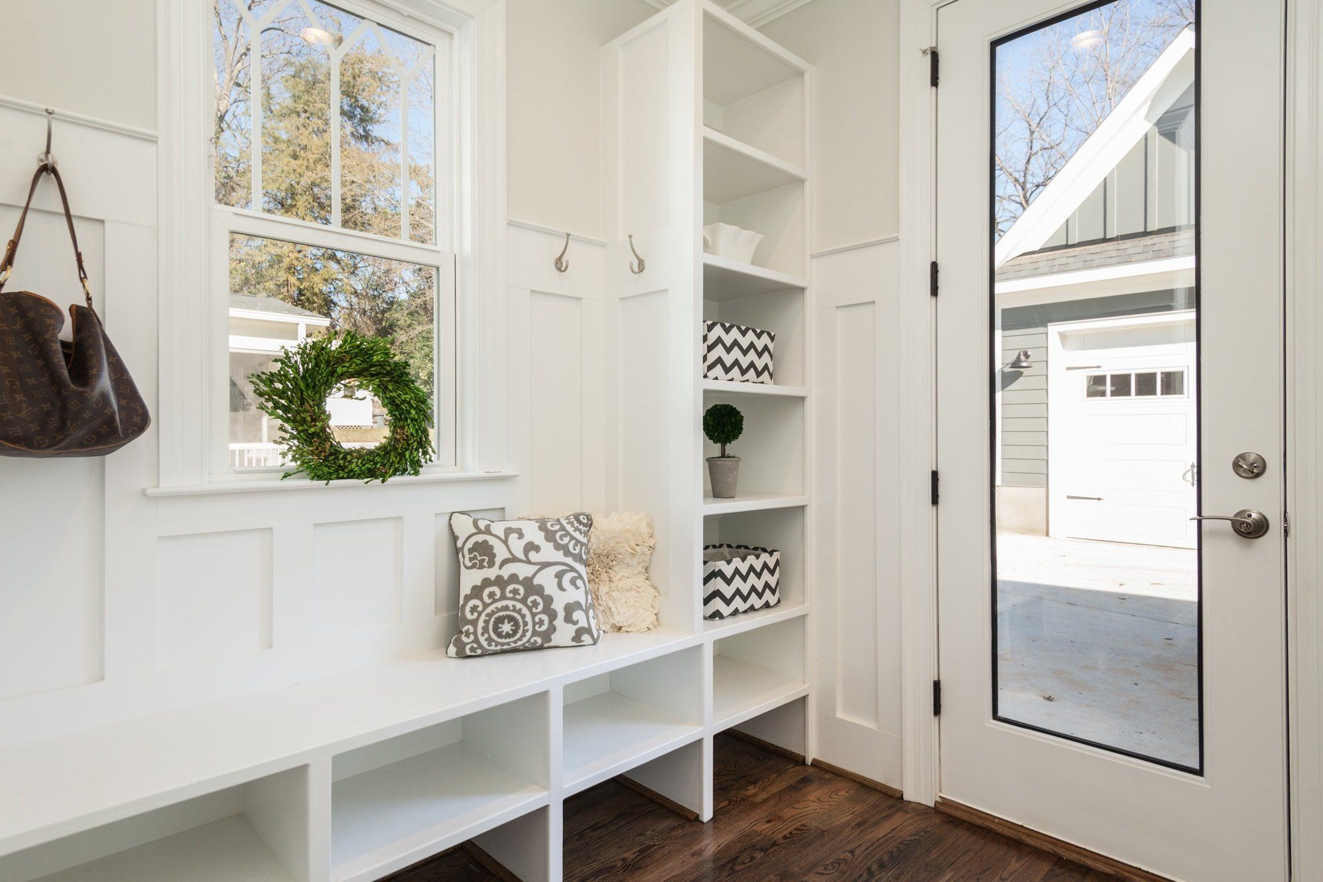A hallway with a bench , shelves , a mirror and a window.