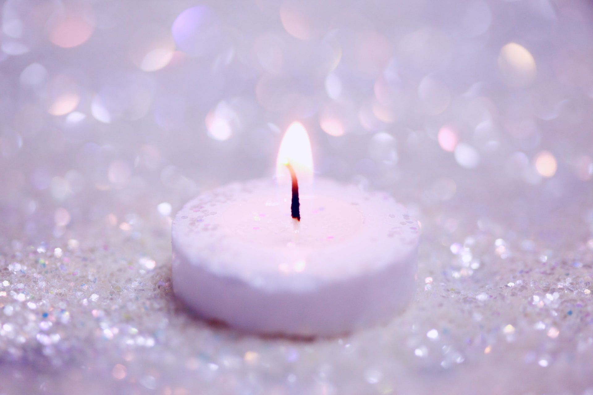 A small white candle is lit on a purple background.