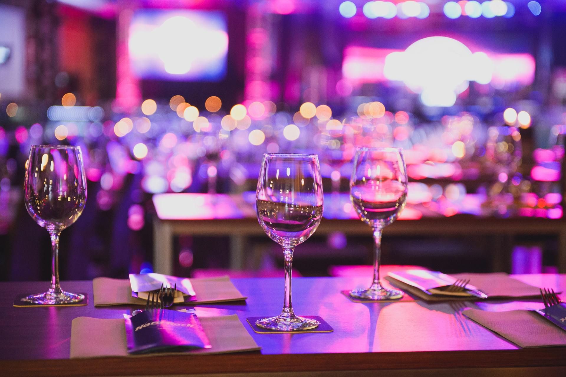 Two wine glasses on a table with purple lights in the background