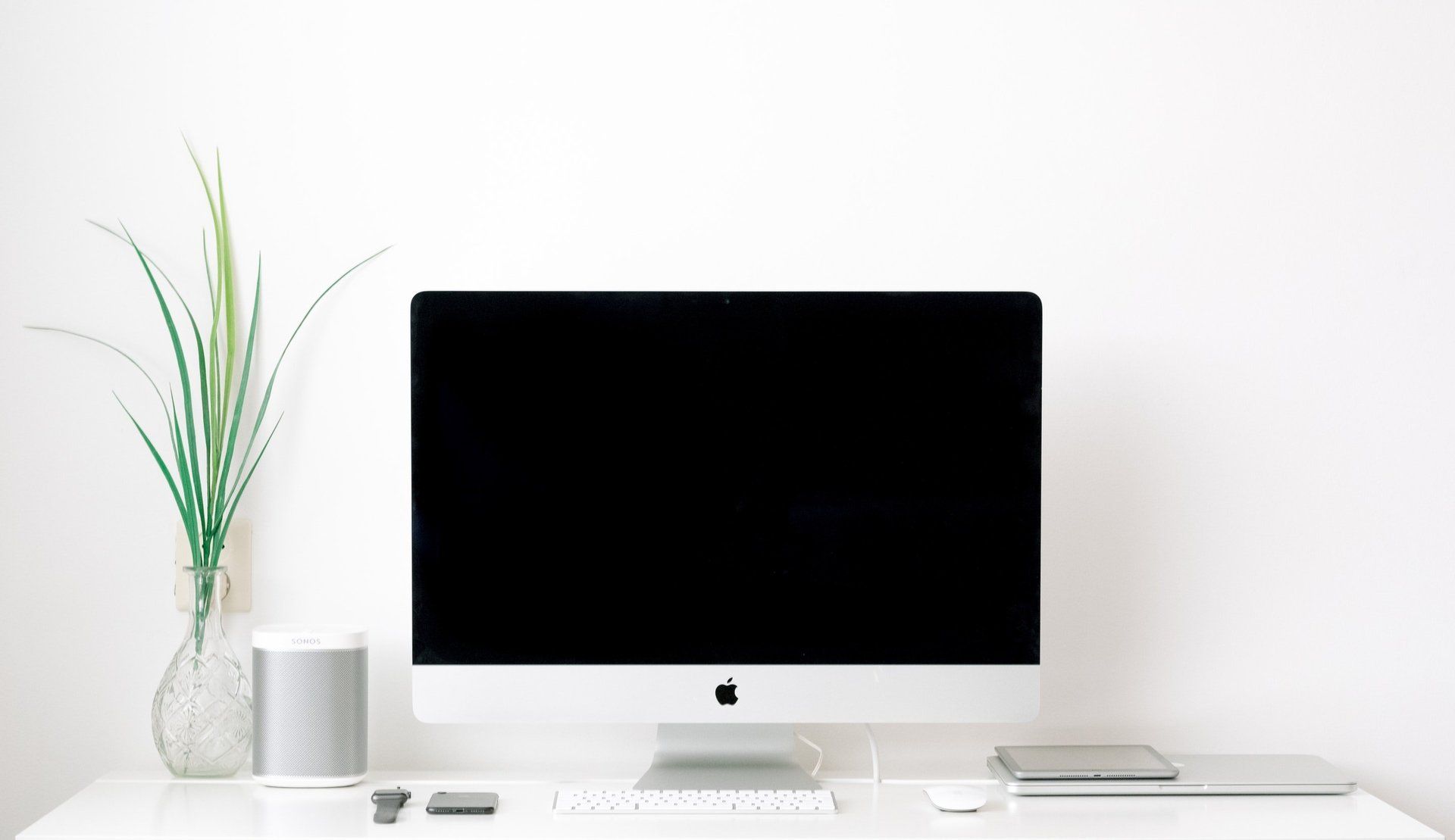 A computer monitor is sitting on top of a white desk next to a plant.