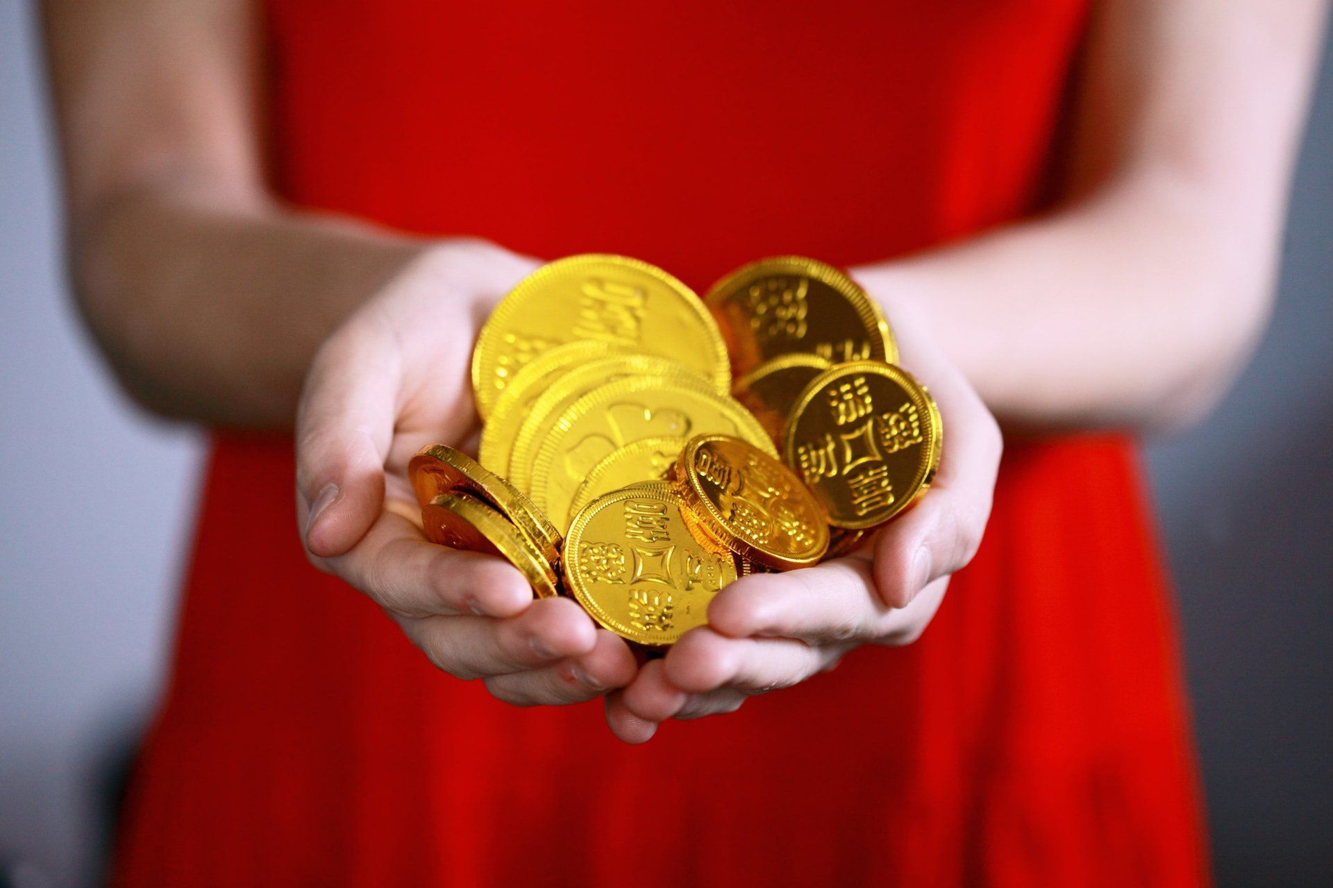 A woman in a red dress is holding a pile of gold coins in her hands.
