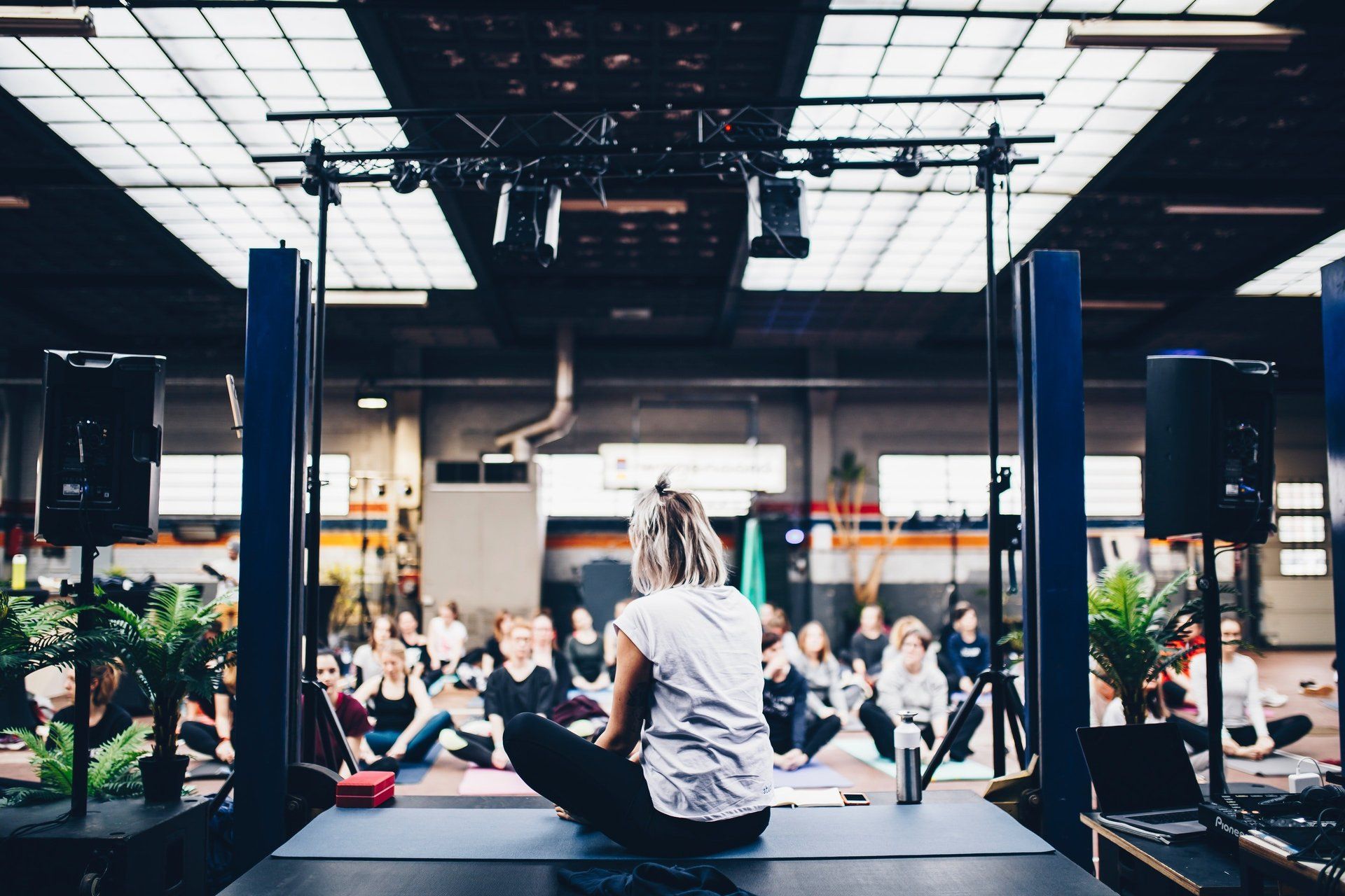 Woman on stage leads a seated group in a light-filled industrial space.