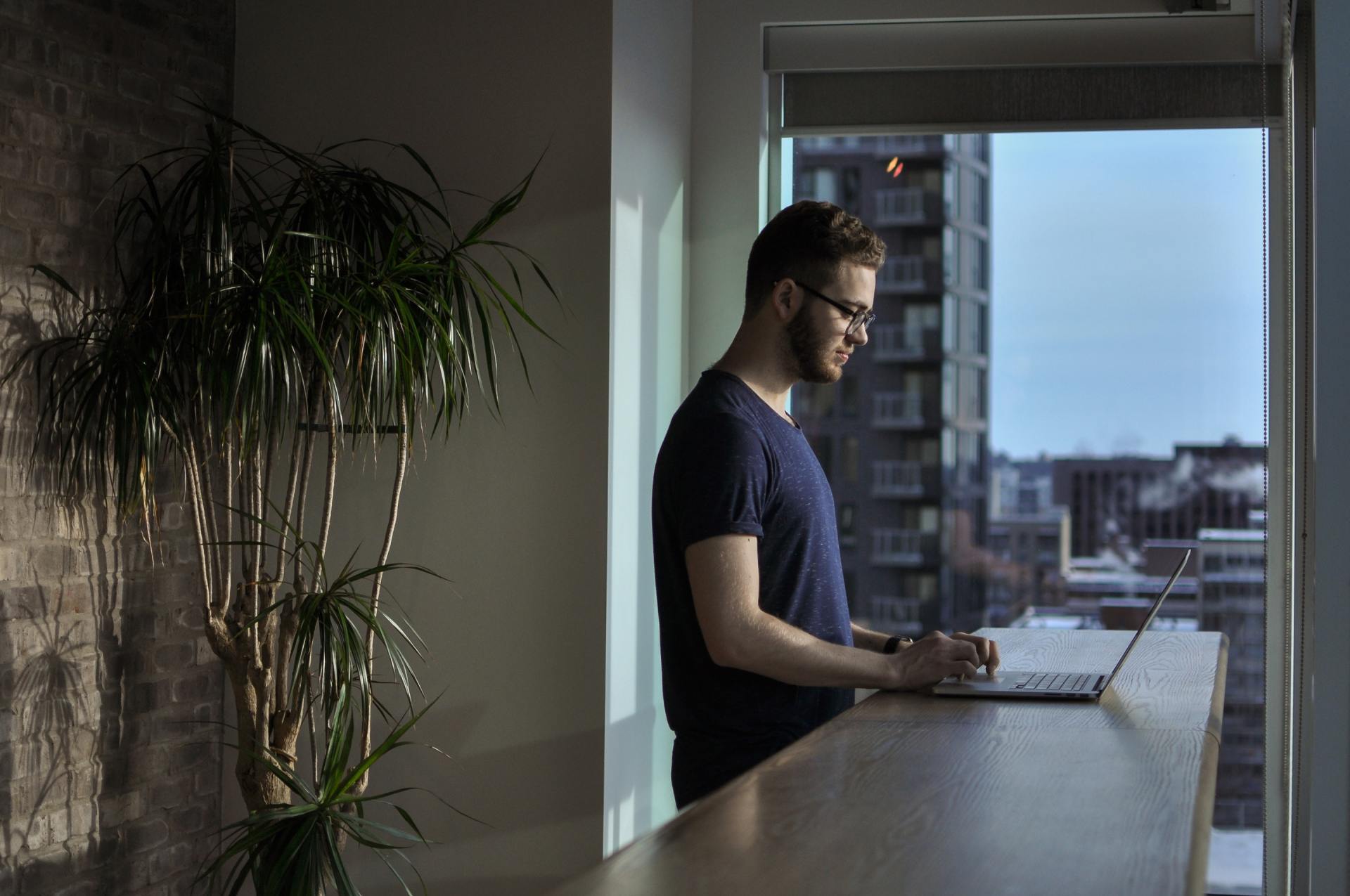 A man is standing at a table using a laptop computer.