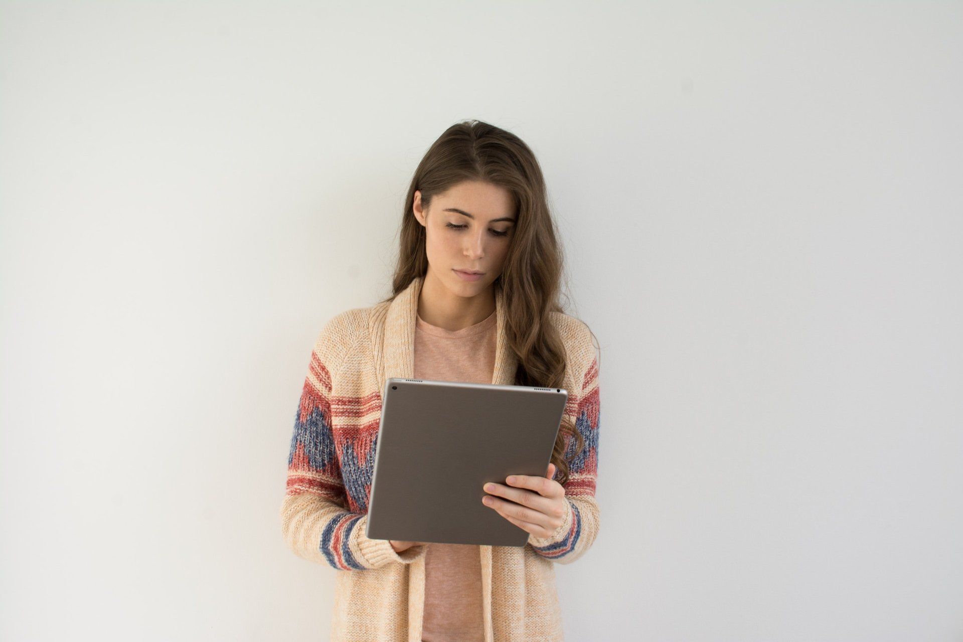 A woman is standing in front of a white wall holding a tablet computer.