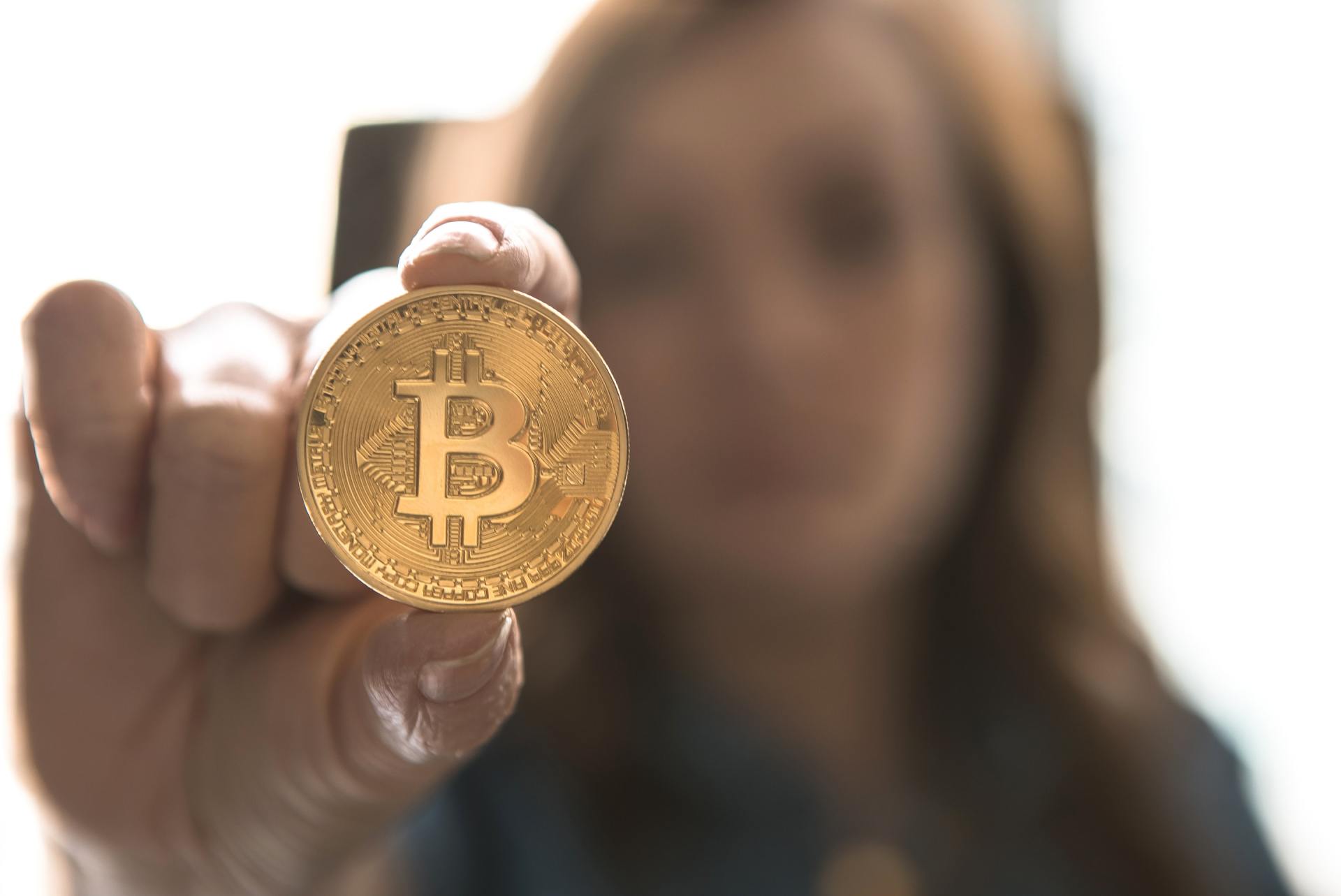 A woman is holding a gold coin with the letter b on it.