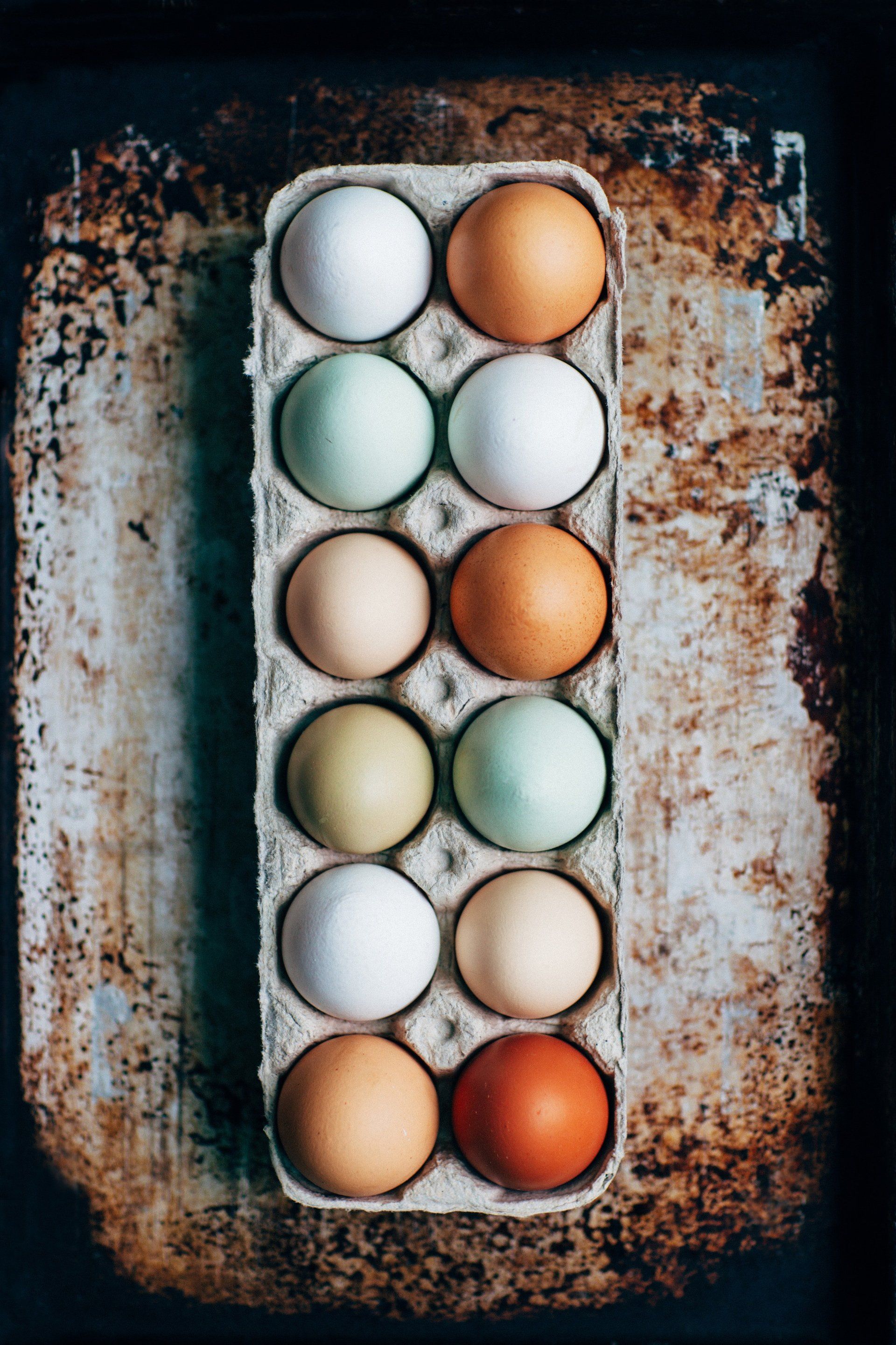A carton of eggs sits on a rusty, textured surface.