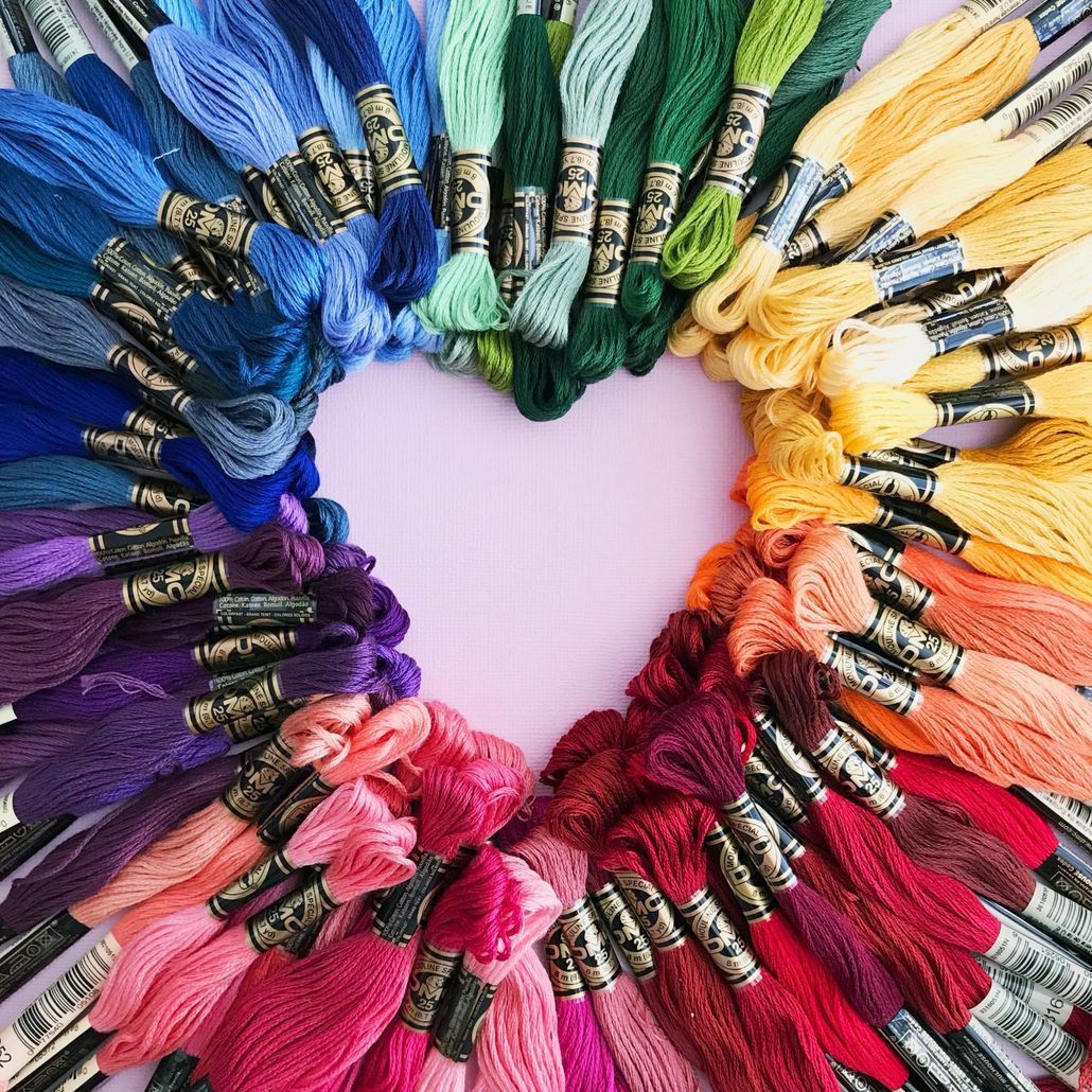 A bunch of different colored embroidery floss are arranged in a circle on a pink surface.