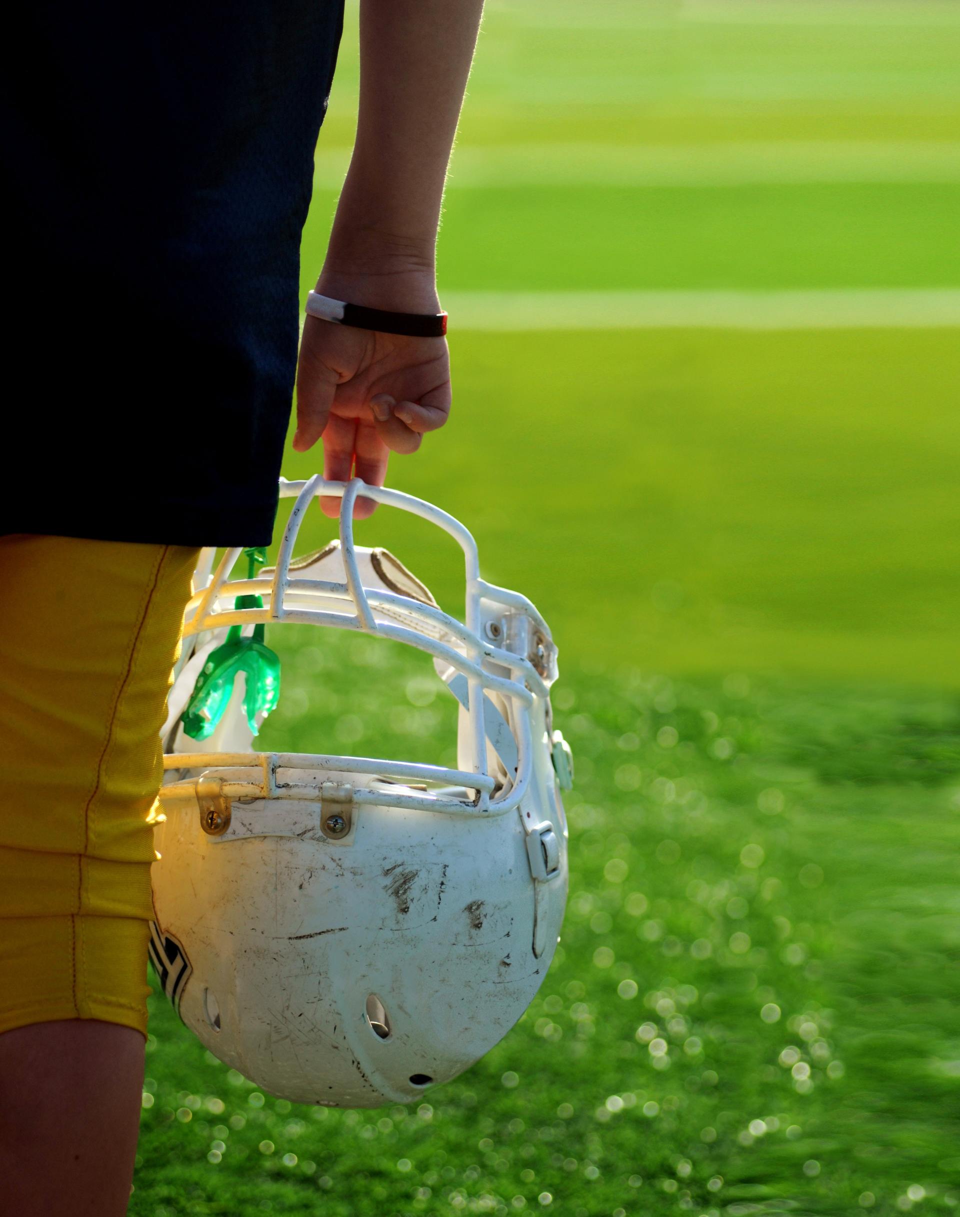 Person holding a white football helmet on a green field.