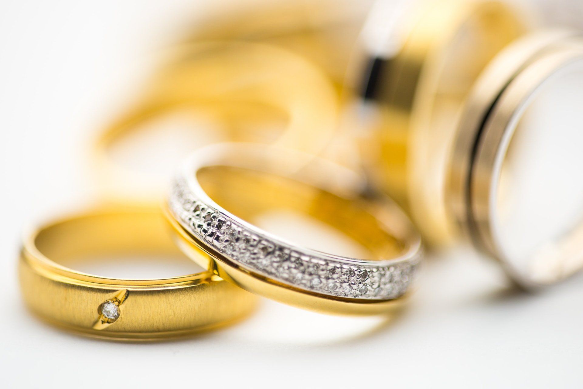 A group of gold wedding rings are stacked on top of each other on a white surface.