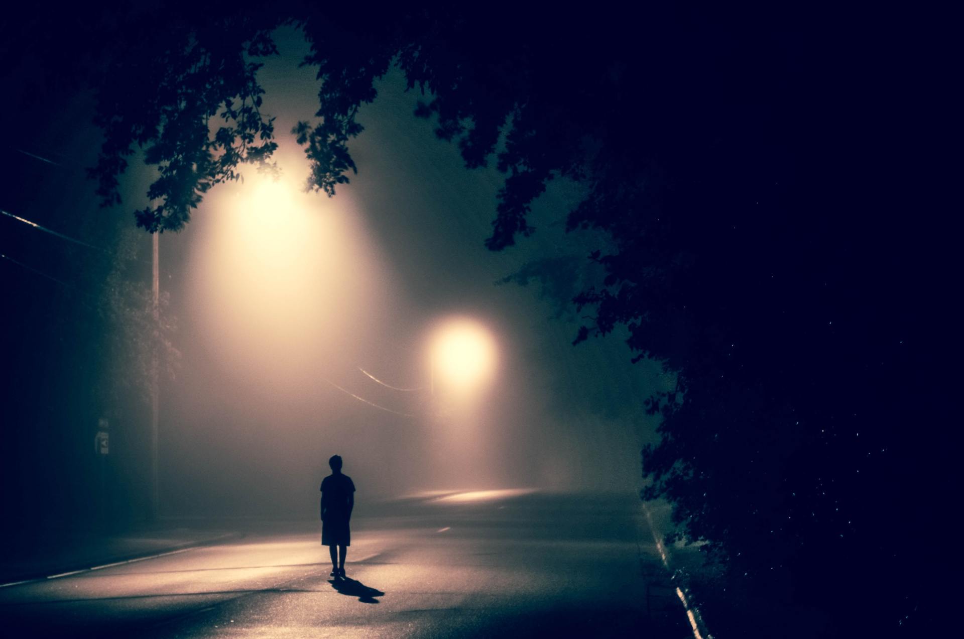 A man is walking down a foggy street at night.