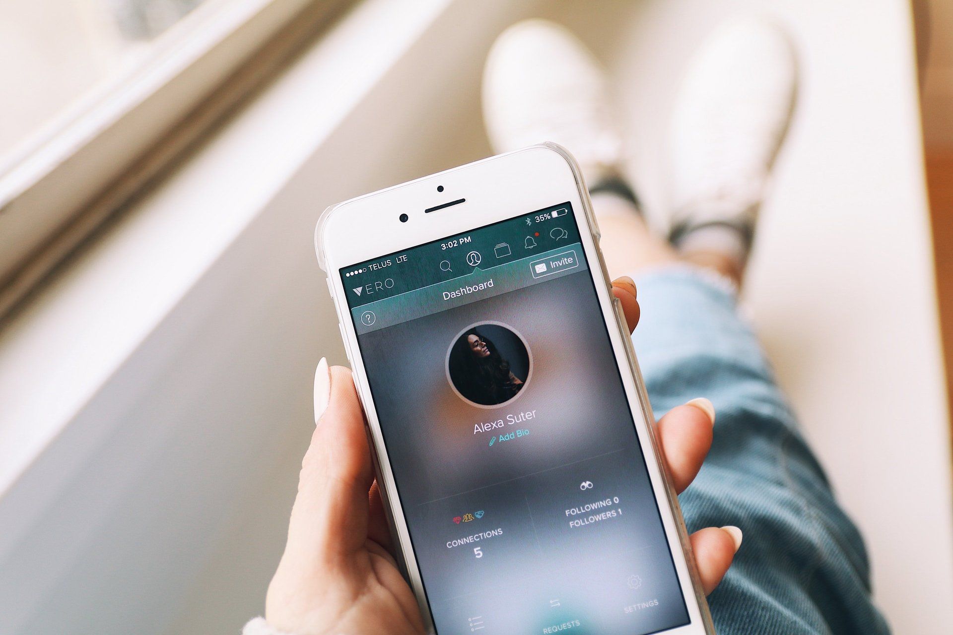 Person holding a smartphone displaying an app. White sneakers and blue jeans visible in the background.