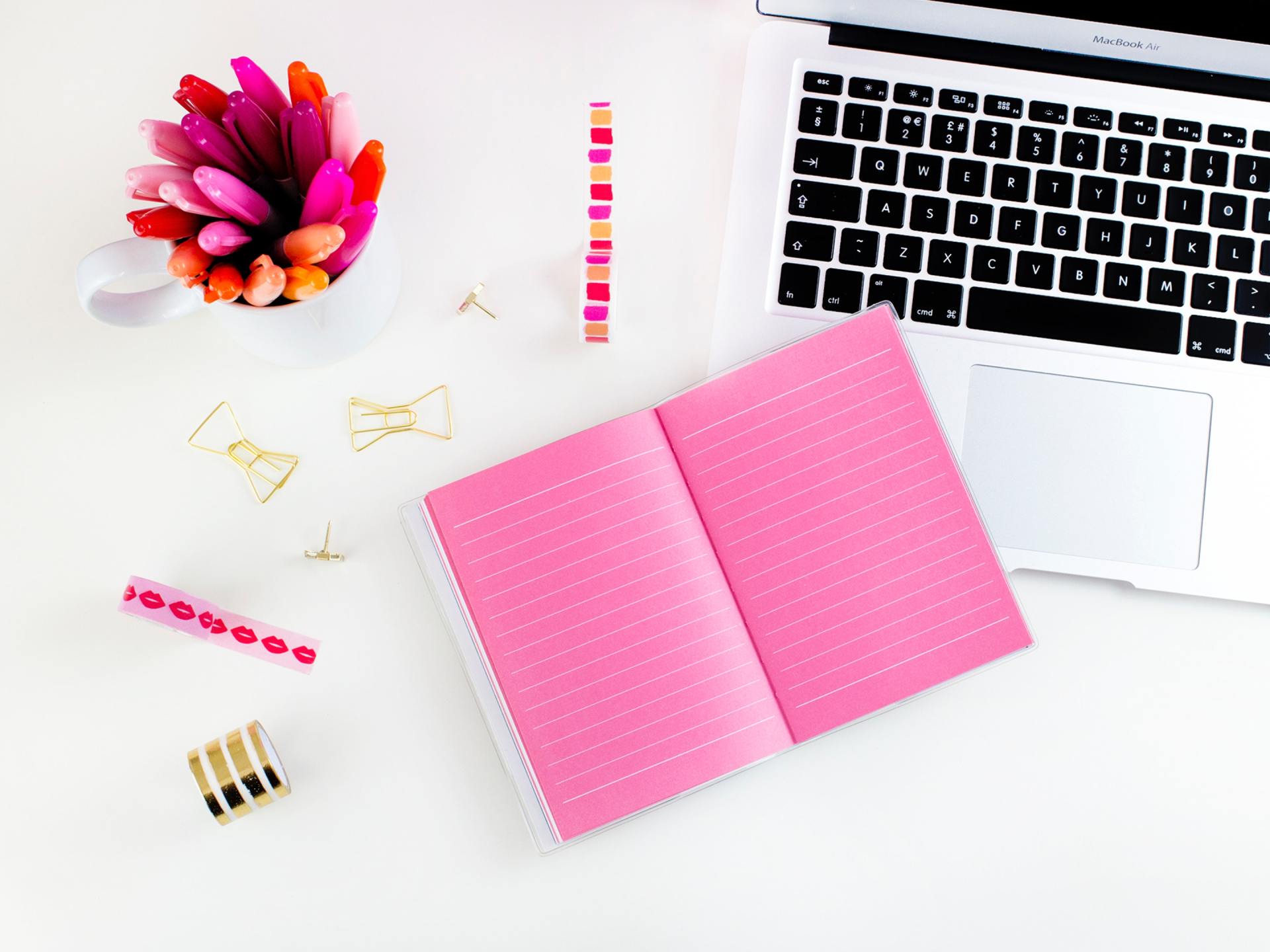 A pink notebook is open next to a laptop