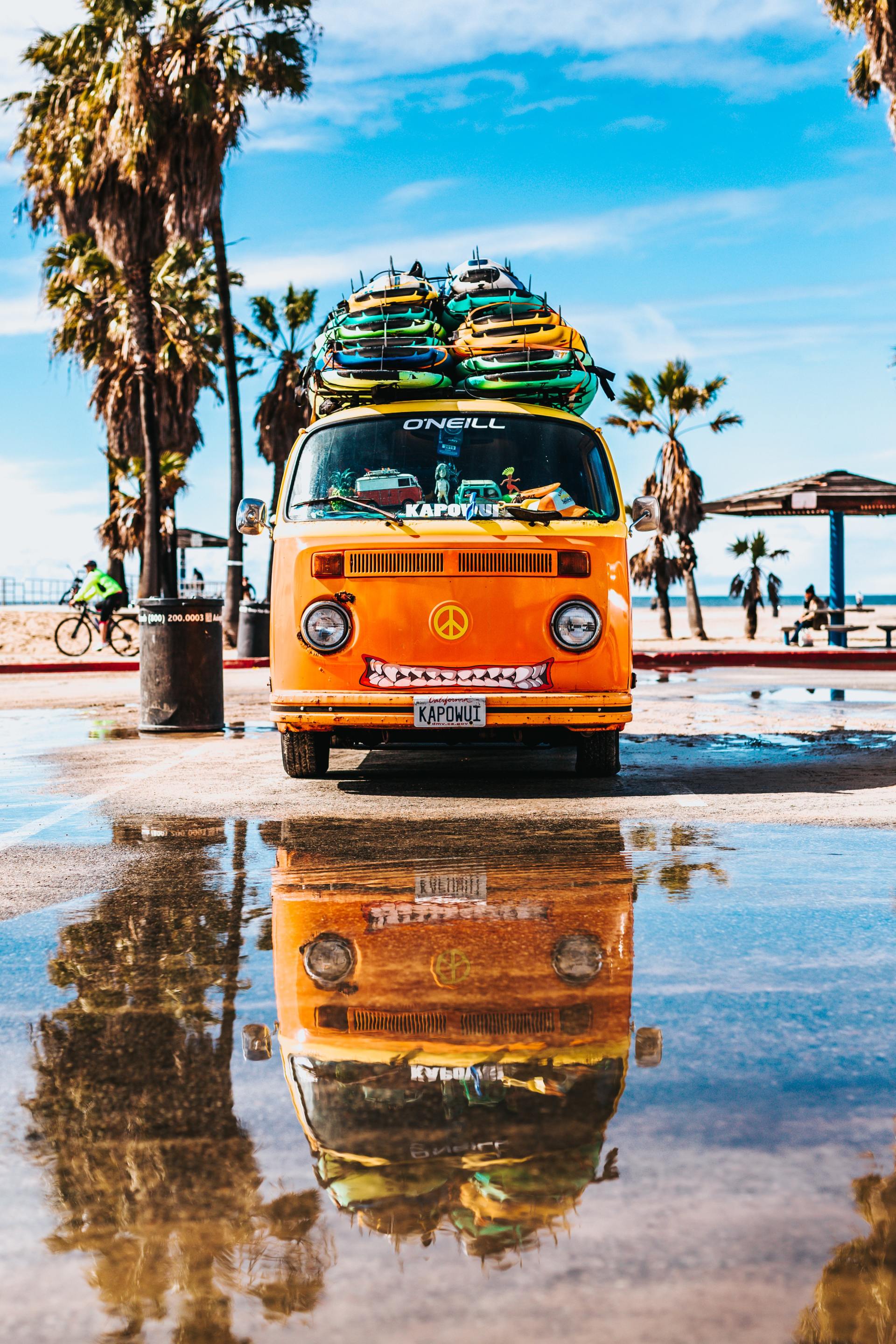 An orange van with surfboards on top of it is parked on the beach