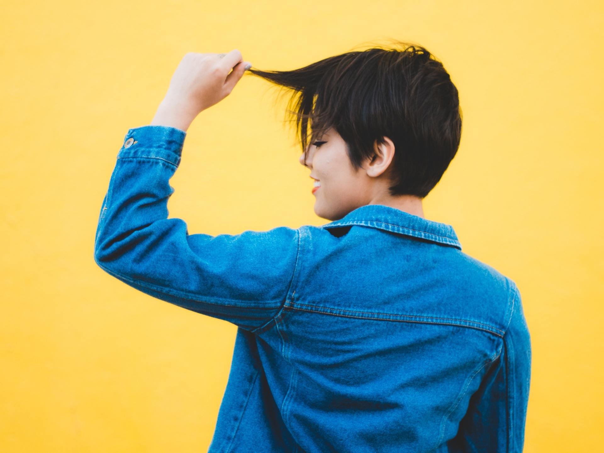 A person is touching their hair with a bright yellow background.