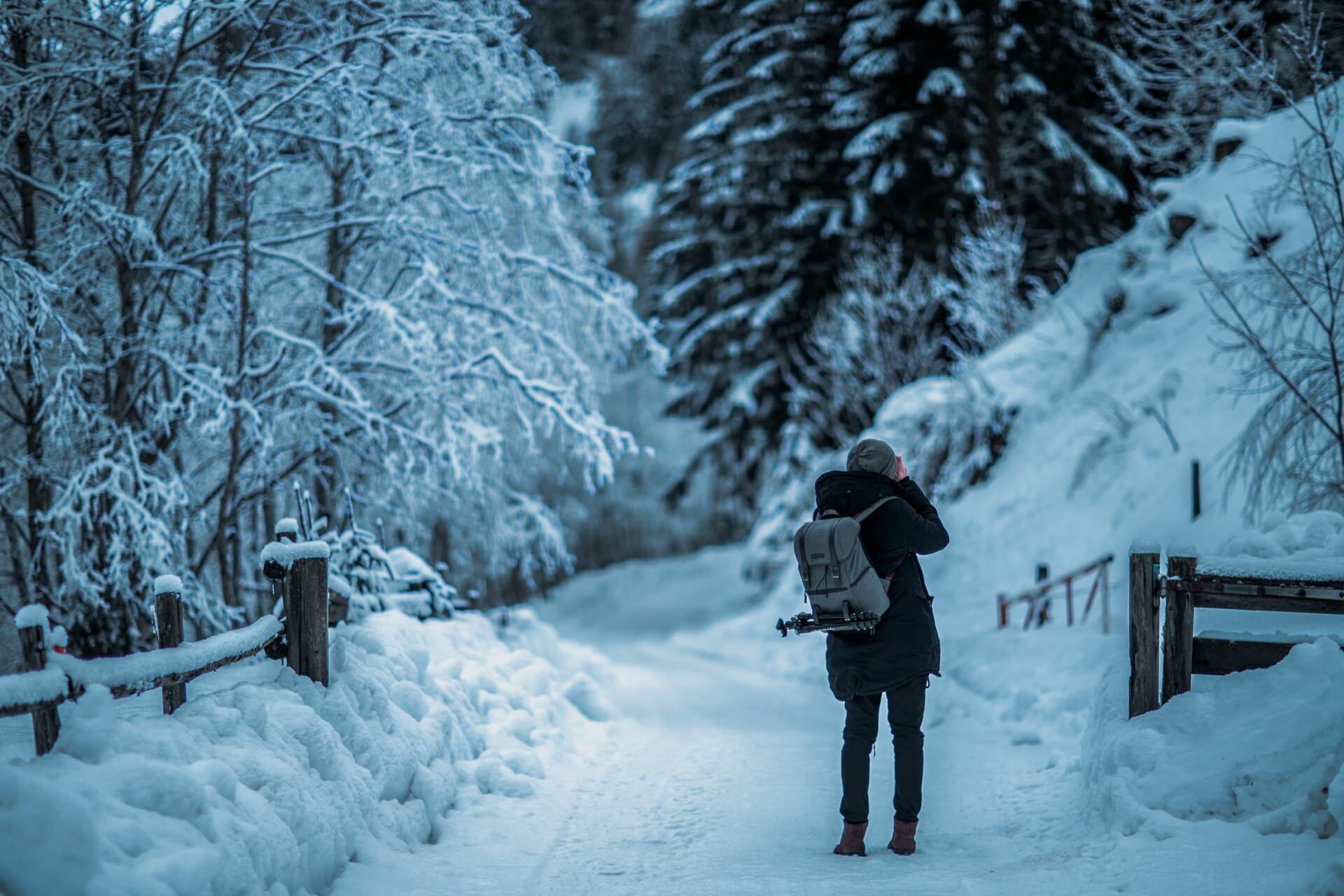Eine Person mit Rucksack geht auf einem verschneiten Waldweg, umgeben von frostbedeckten Bäumen.