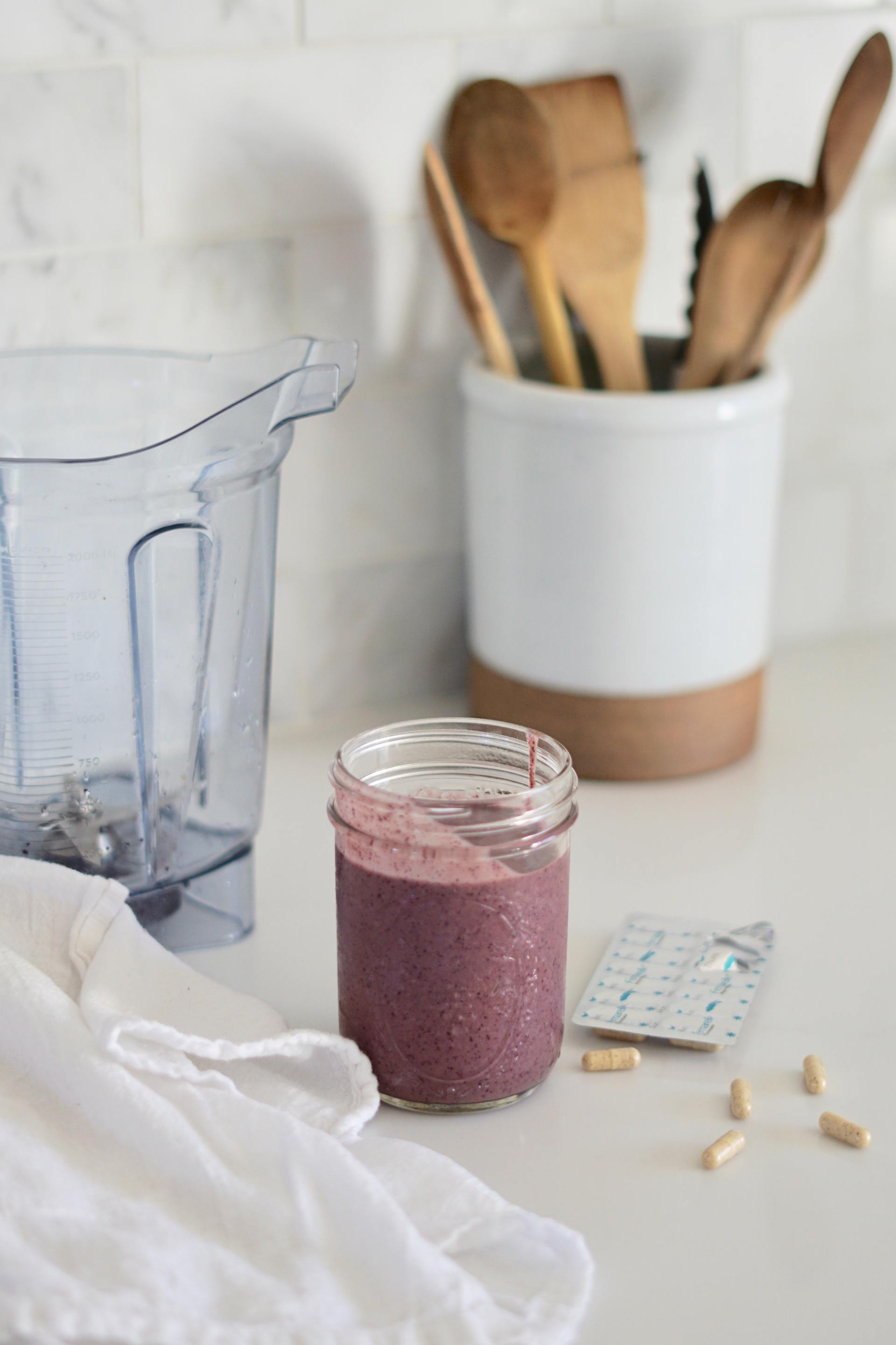 A jar of smoothie is sitting on a counter next to a blender.