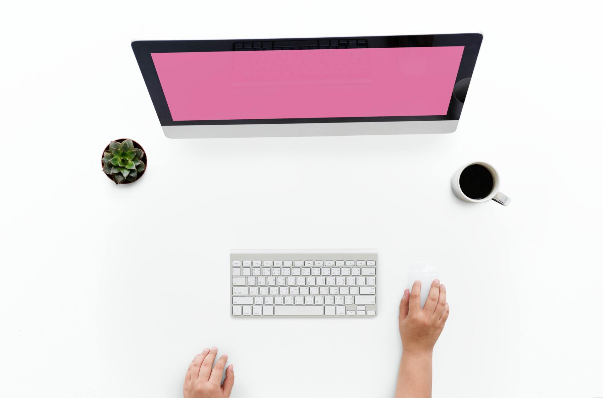 A person is sitting at a desk using a computer with a pink screen.