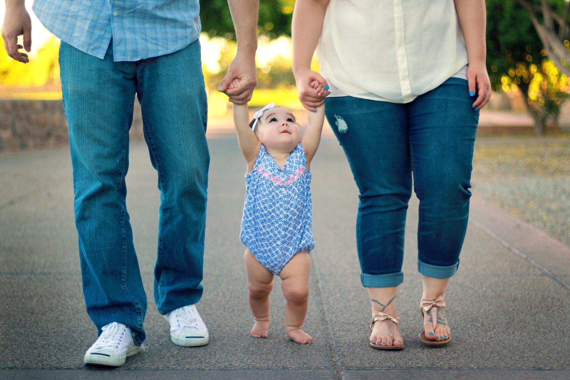 A man and woman are holding a baby 's hand while walking down a road.