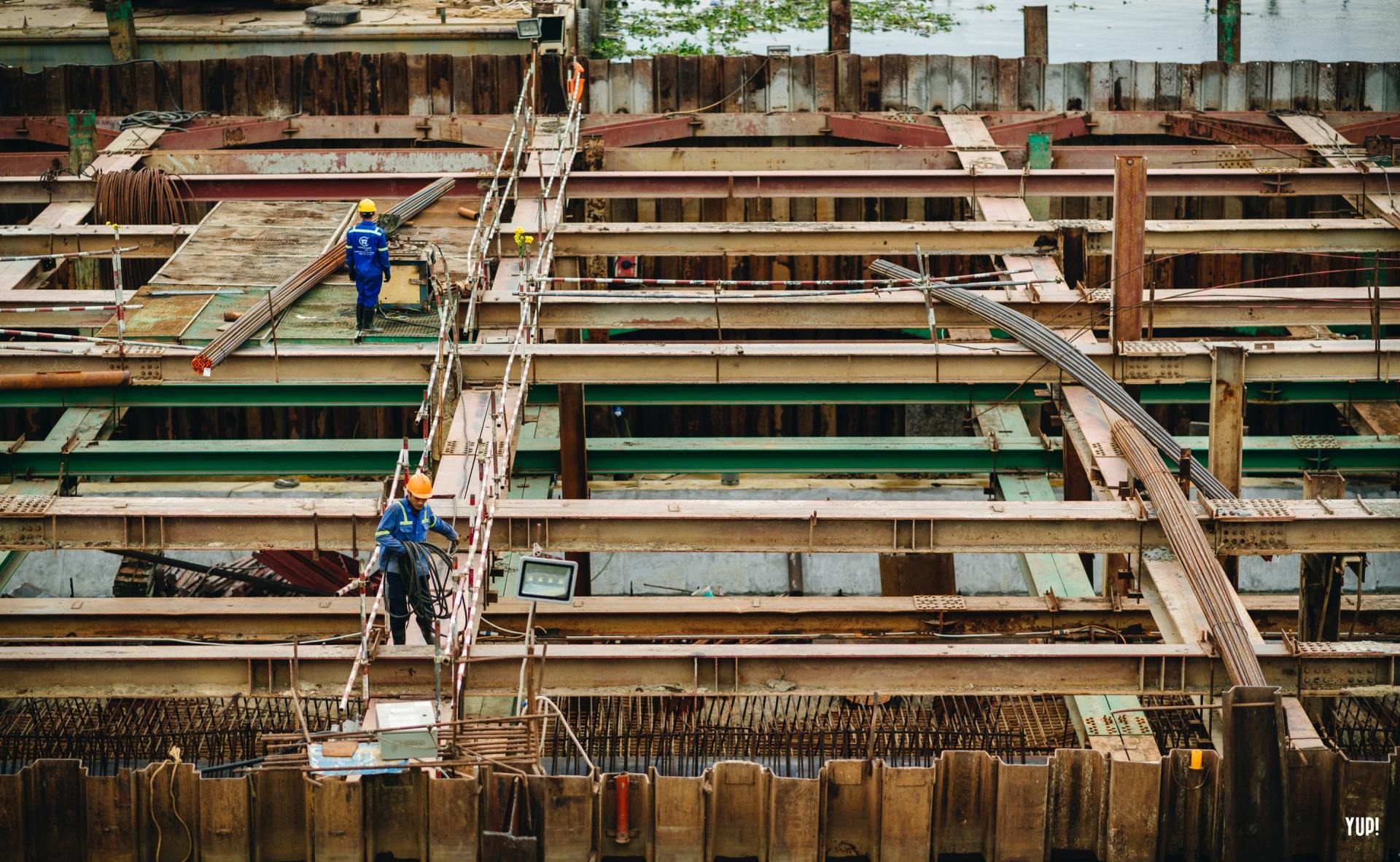 Des ouvriers du bâtiment travaillent sur un chantier à structure métallique, avec des poutres et des échafaudages visibles.
