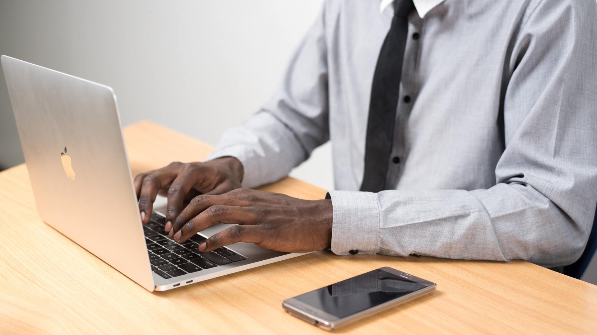 Person typing on a laptop at a desk with a smartphone.