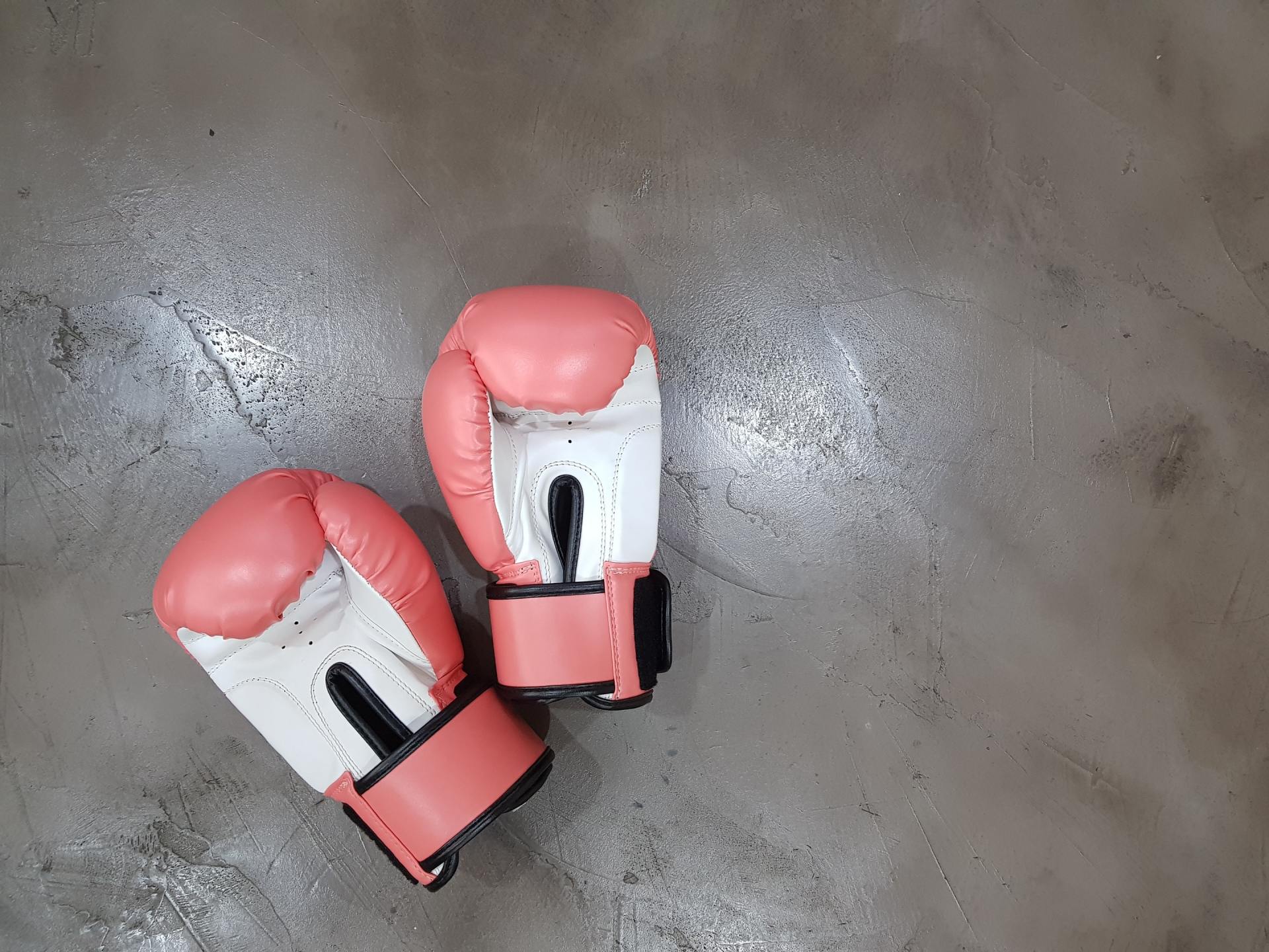 A pair of pink and white boxing gloves are sitting on a concrete floor.