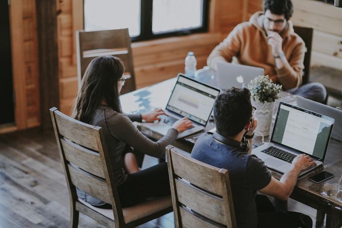 A group of people are sitting around a table with laptops.