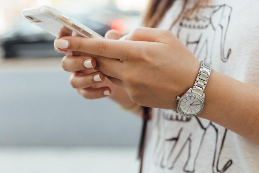 Close-up of hands using a white smartphone, wearing a silver watch and striped shirt.