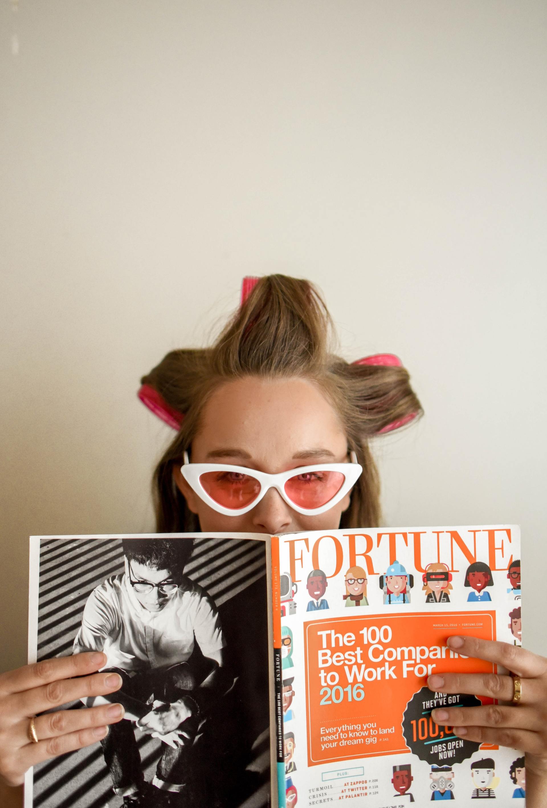 A woman with curlers in her hair is holding a fortune magazine