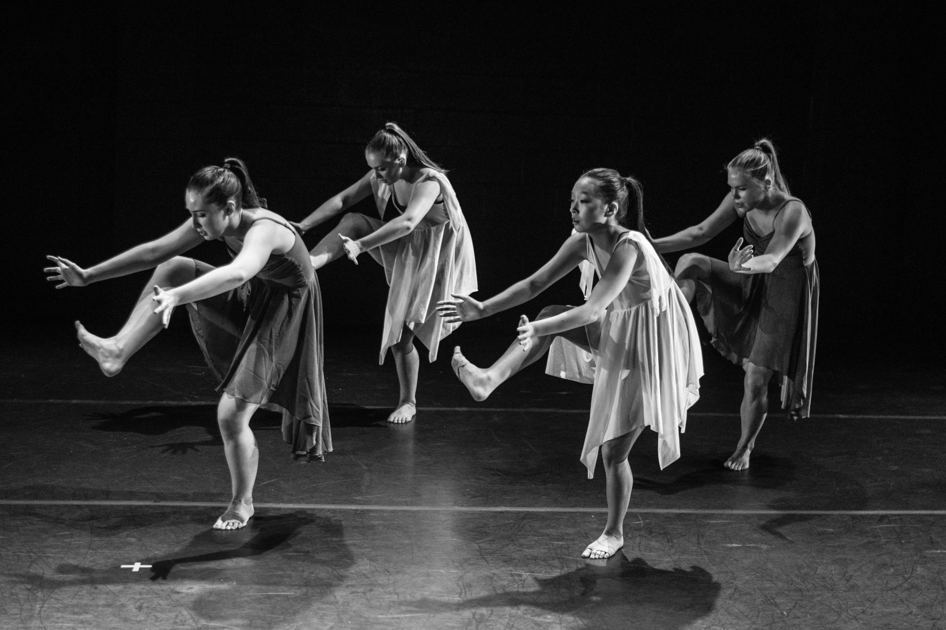 Four female dancers in flowing dresses performing a dance on a stage.