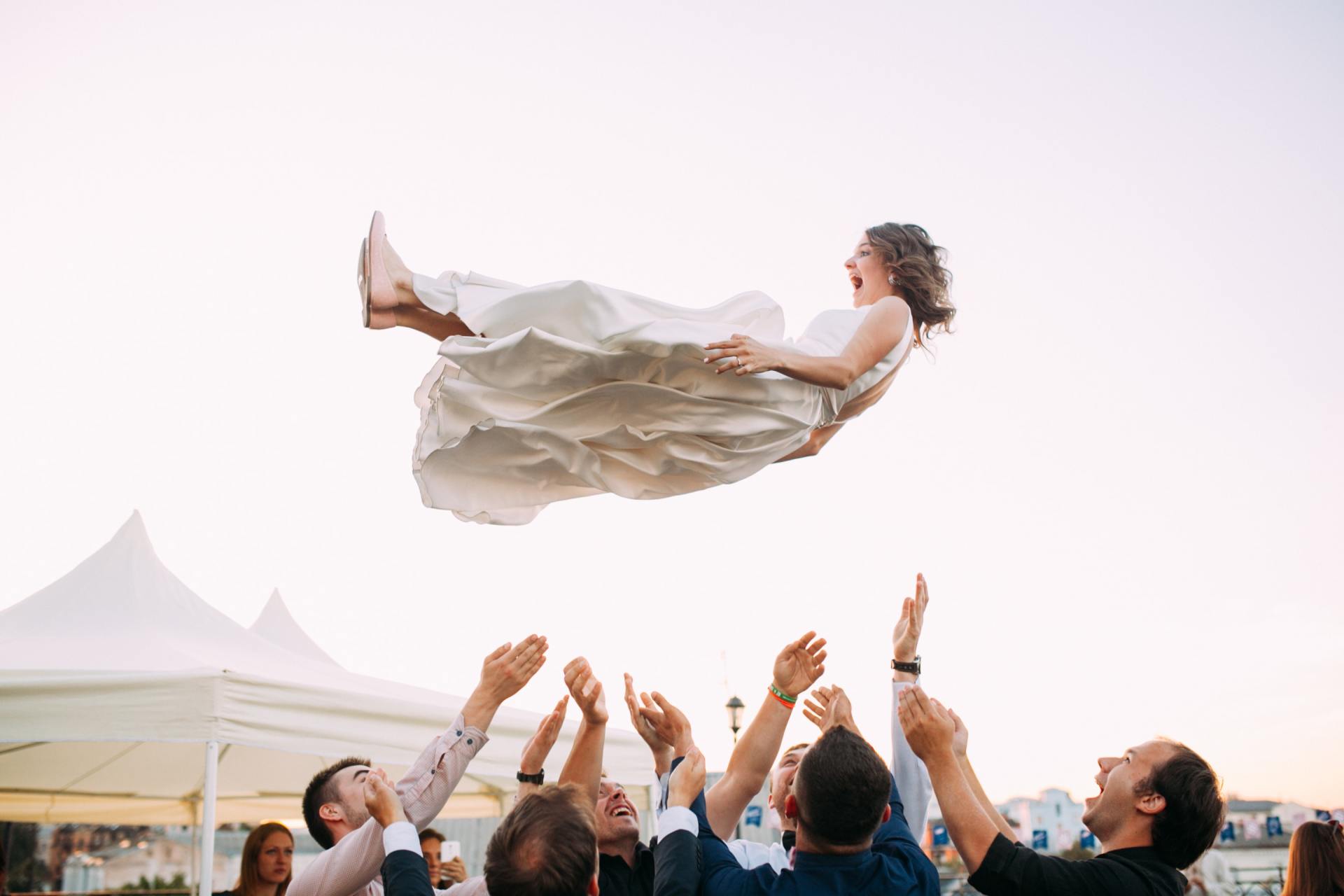 Wedding photo of a bride being thrown up into the air by a group of guests from the wedding.