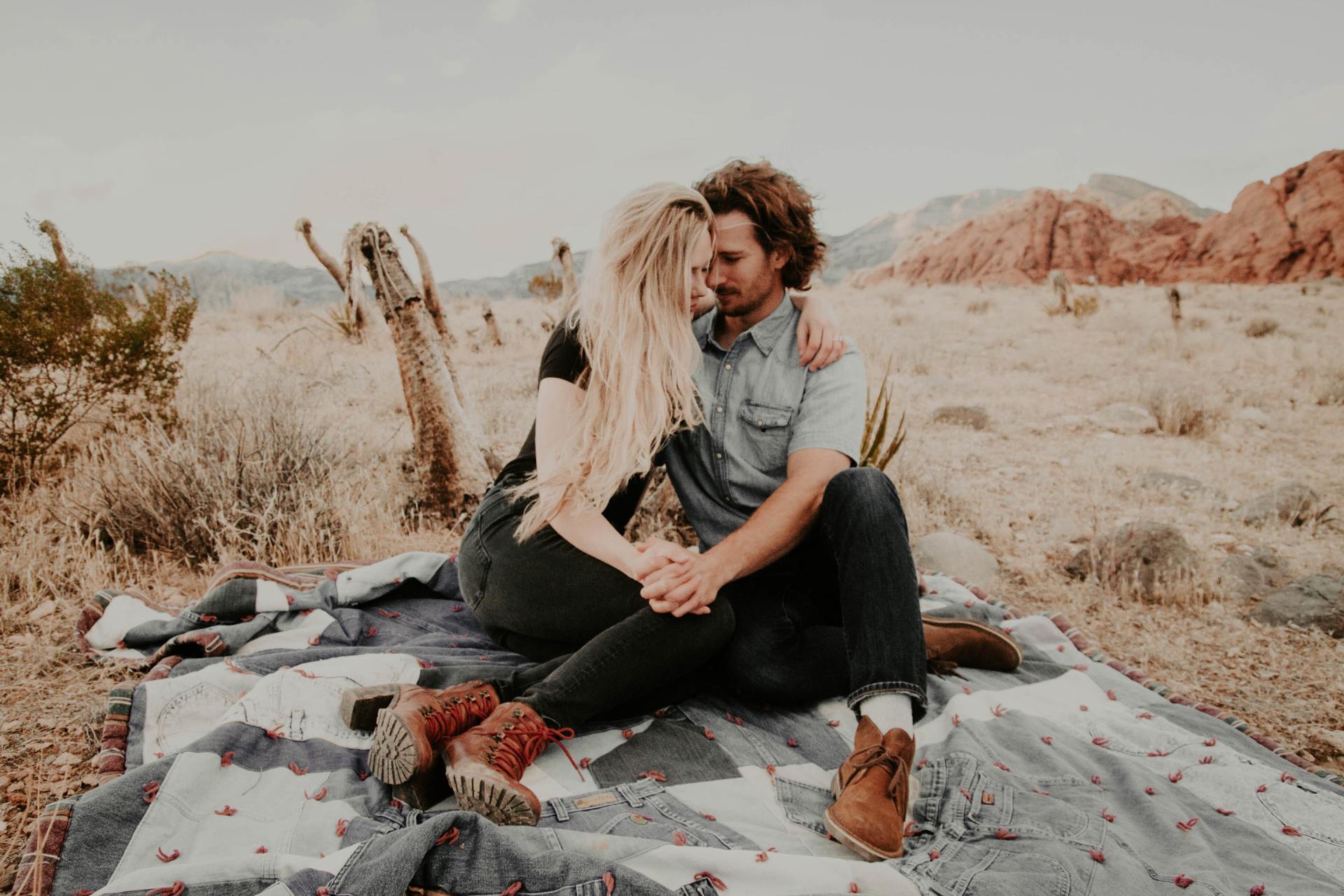 A man and a woman are sitting on a blanket in the desert.