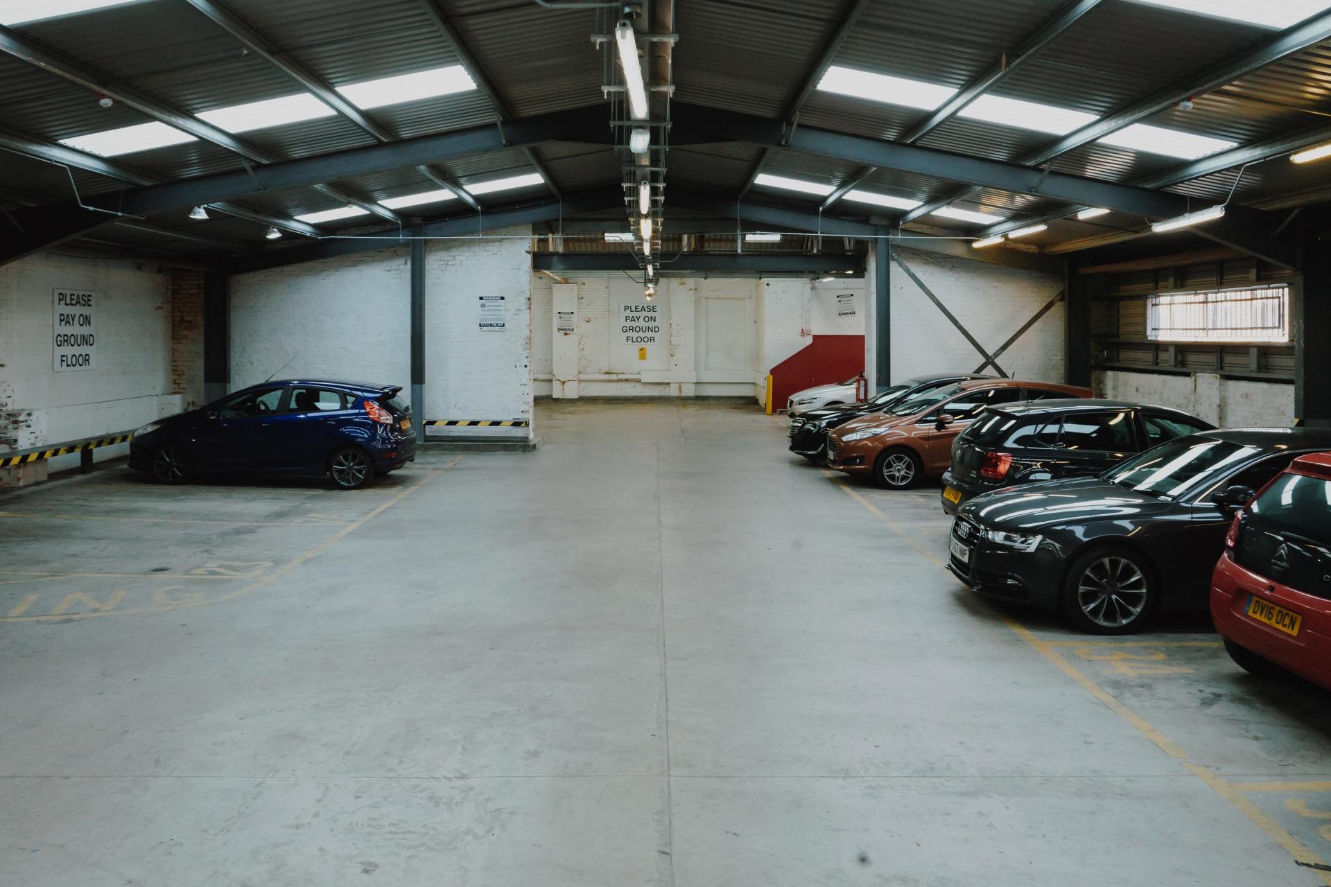 Cars parked inside a large industrial building, gray concrete floor, metal roof with lights.
