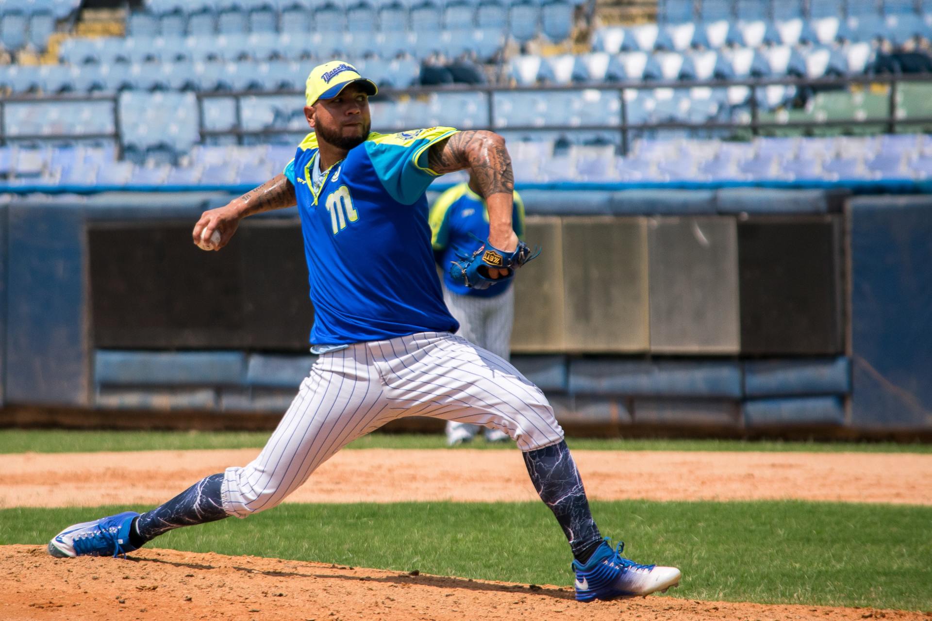 Baseball pitcher in blue and yellow uniform mid-throw on the mound