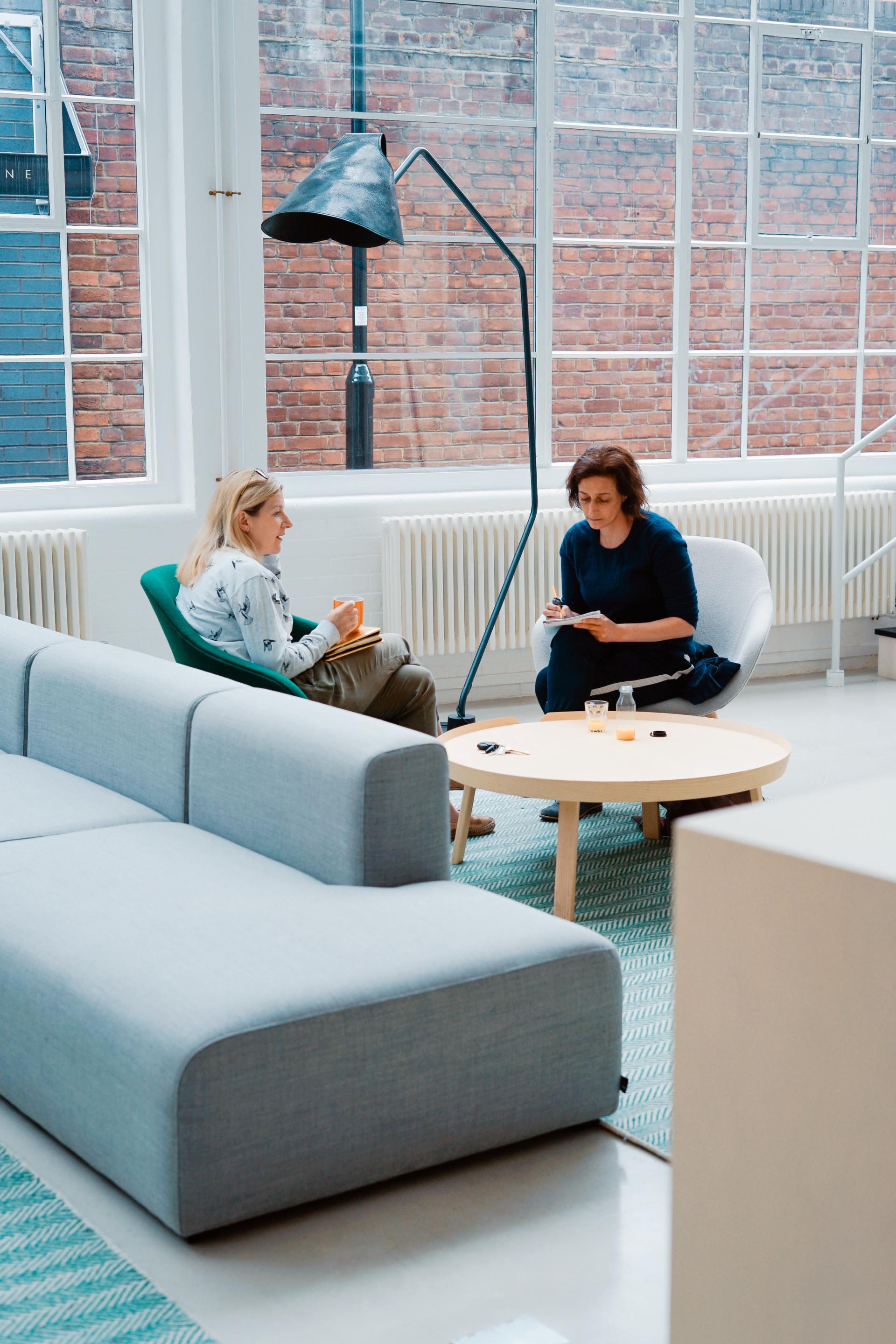 two women chatting sat on chairs in an office setting