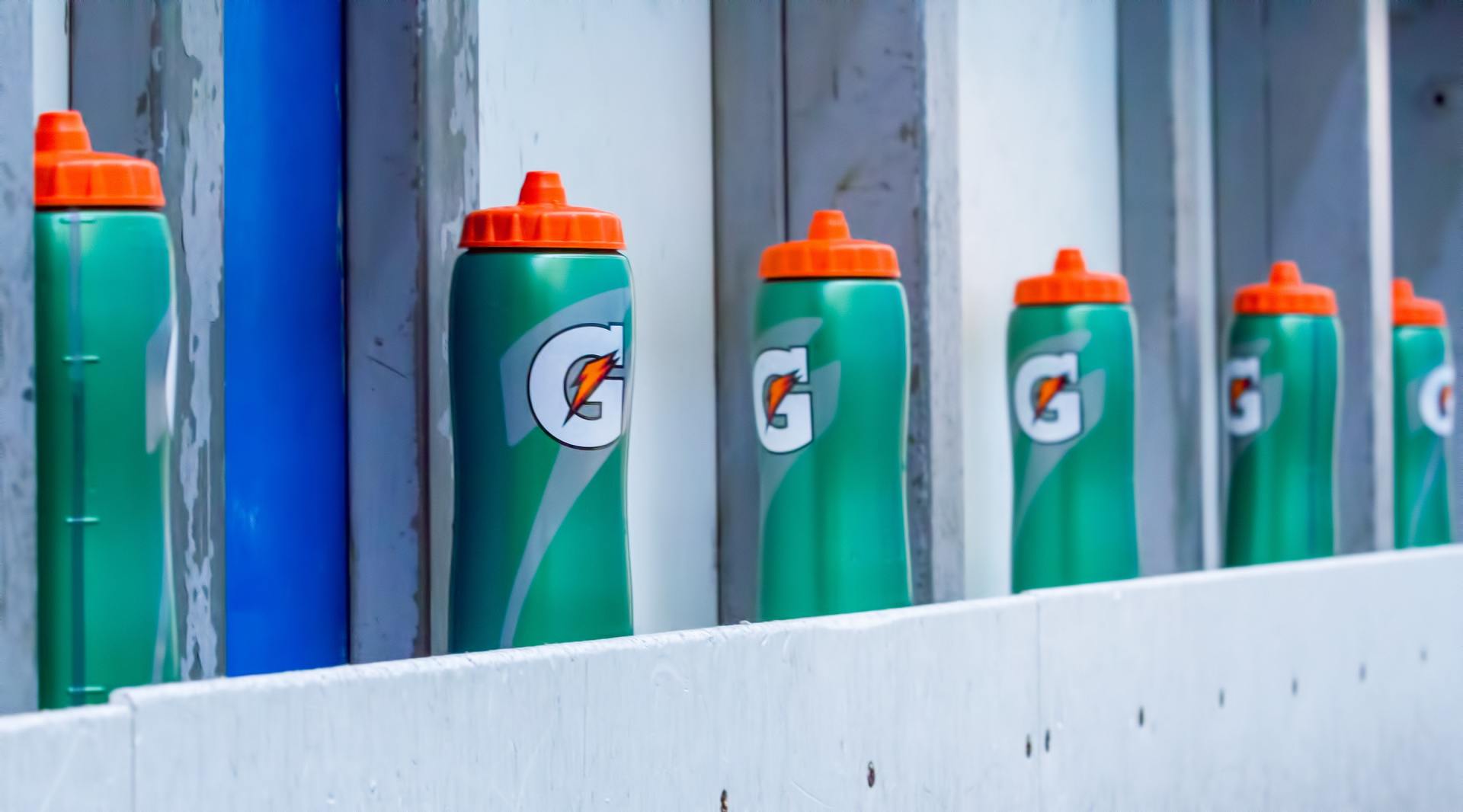 Green Gatorade bottles with orange lids lined up on a white shelf.