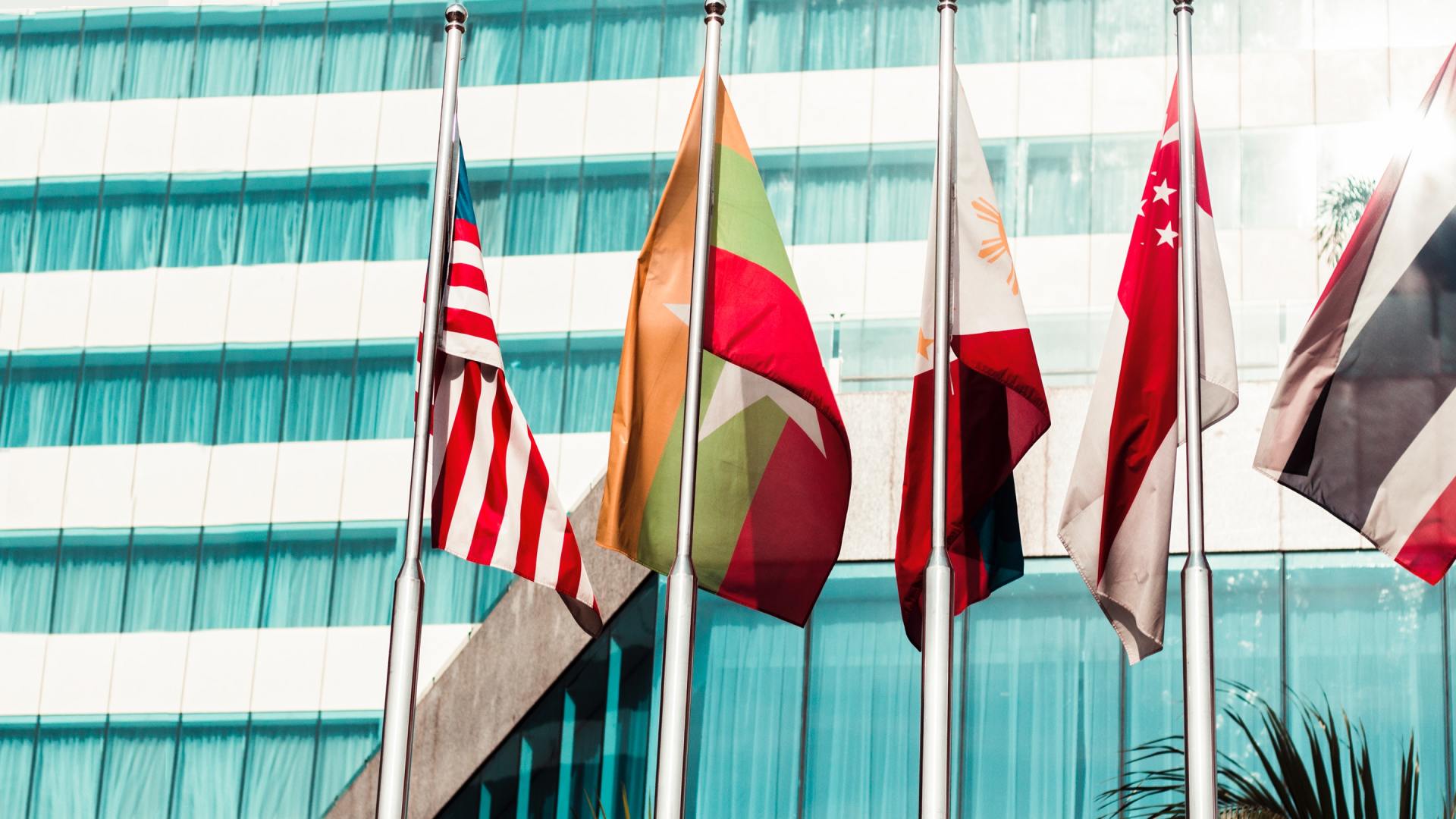 A row of flags are flying in front of a building.