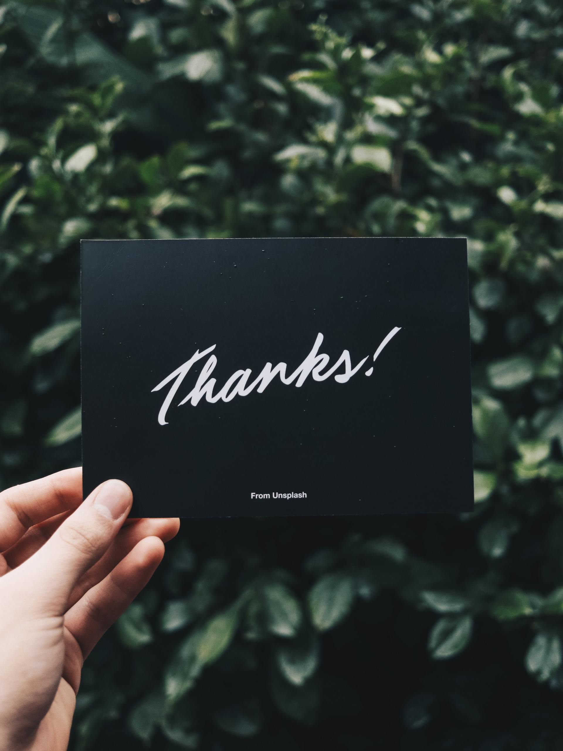 Hand holding a black thank you card with white script