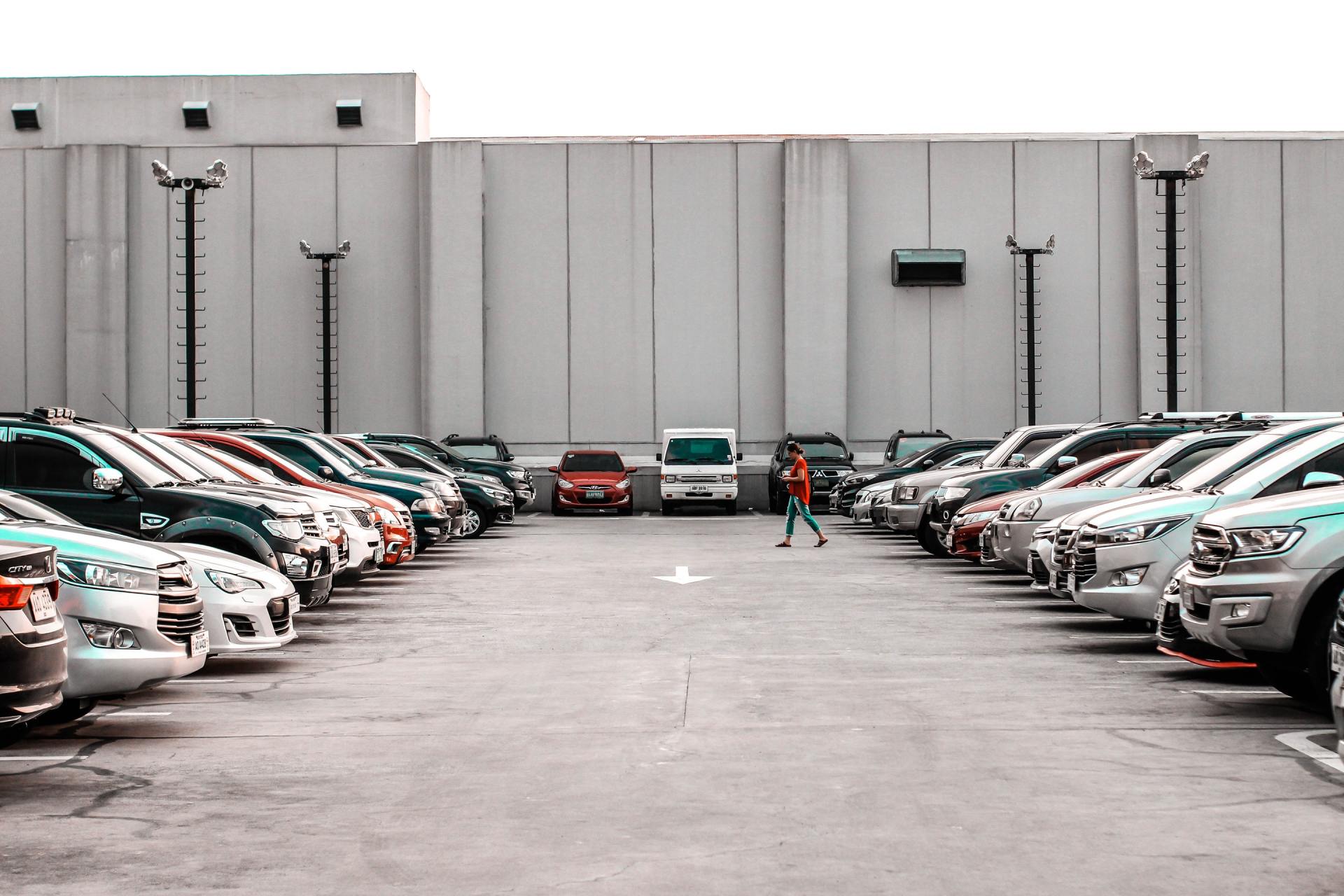Cars parked in rows face a building with a person walking between them.
